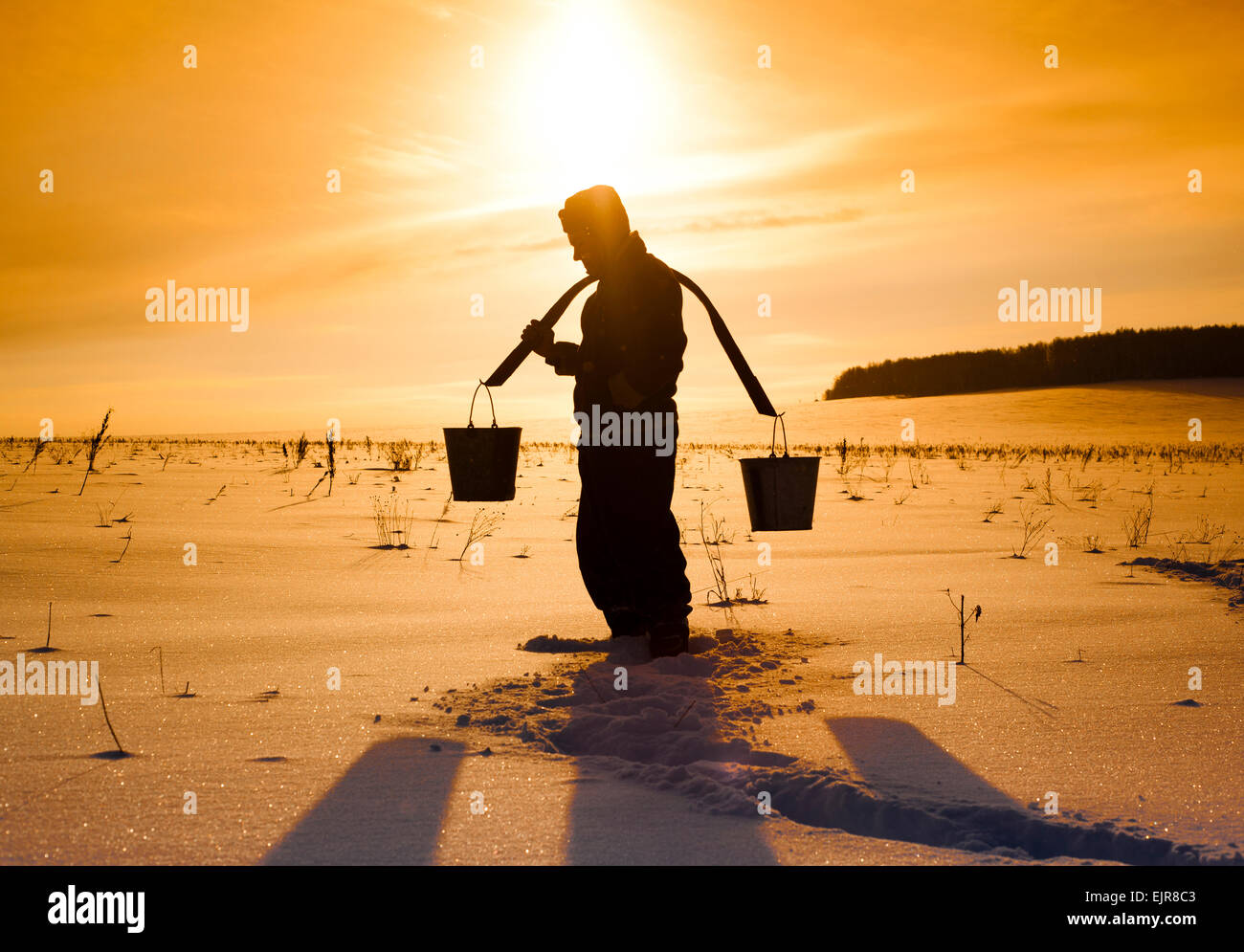 Silhouette of Mari man carrying buckets on traditional yoke in snowy field Stock Photo