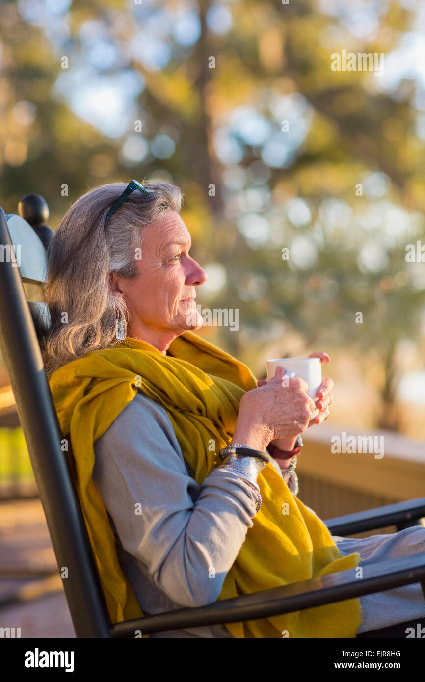 Older Caucasian woman drinking coffee in rocking chair Stock Photo