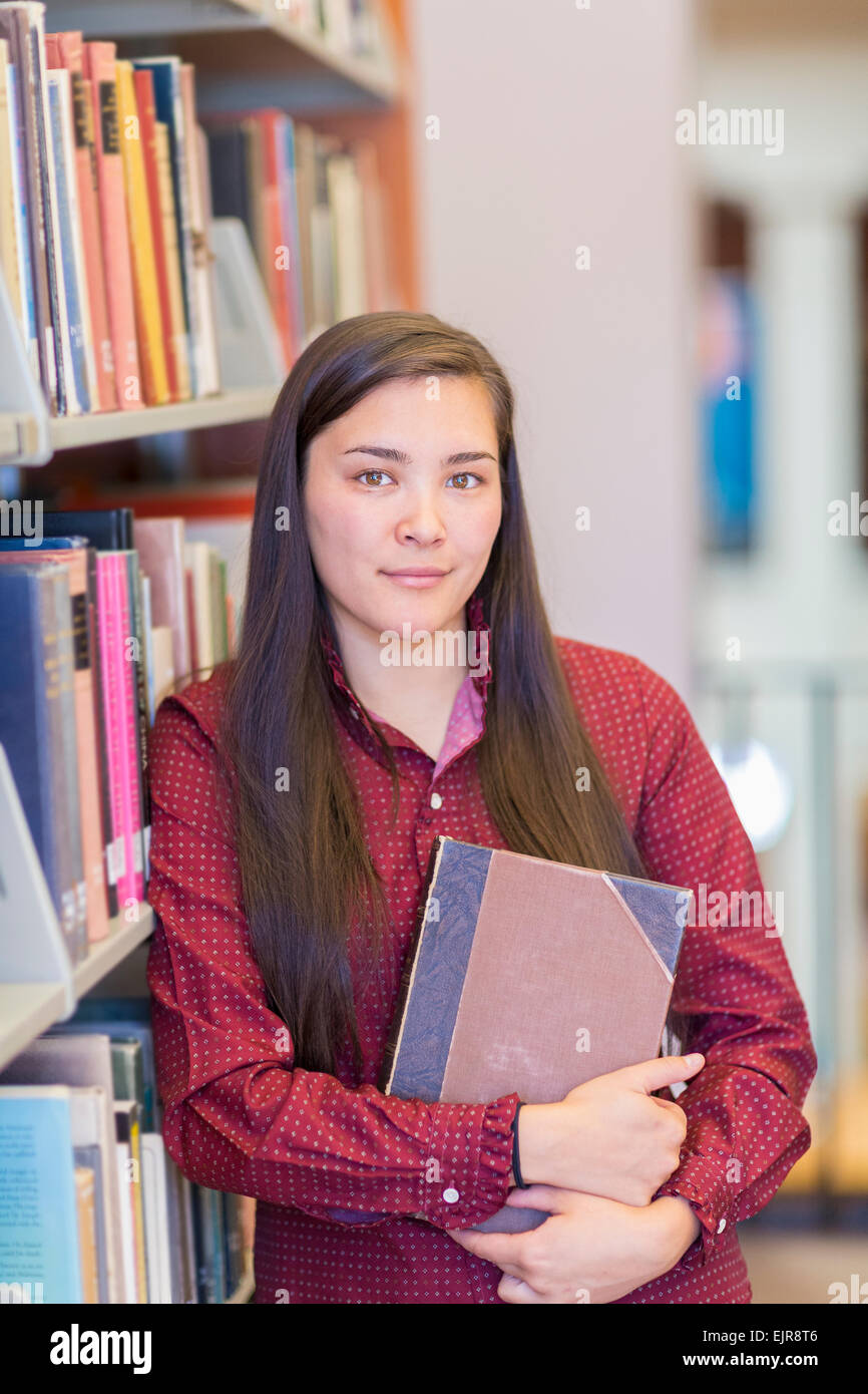 Mixed race student holding book in library Stock Photo Alamy