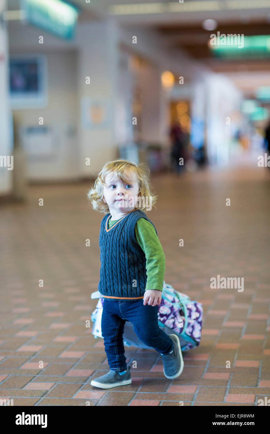 Caucasian baby boy rolling luggage in airport Stock Photo