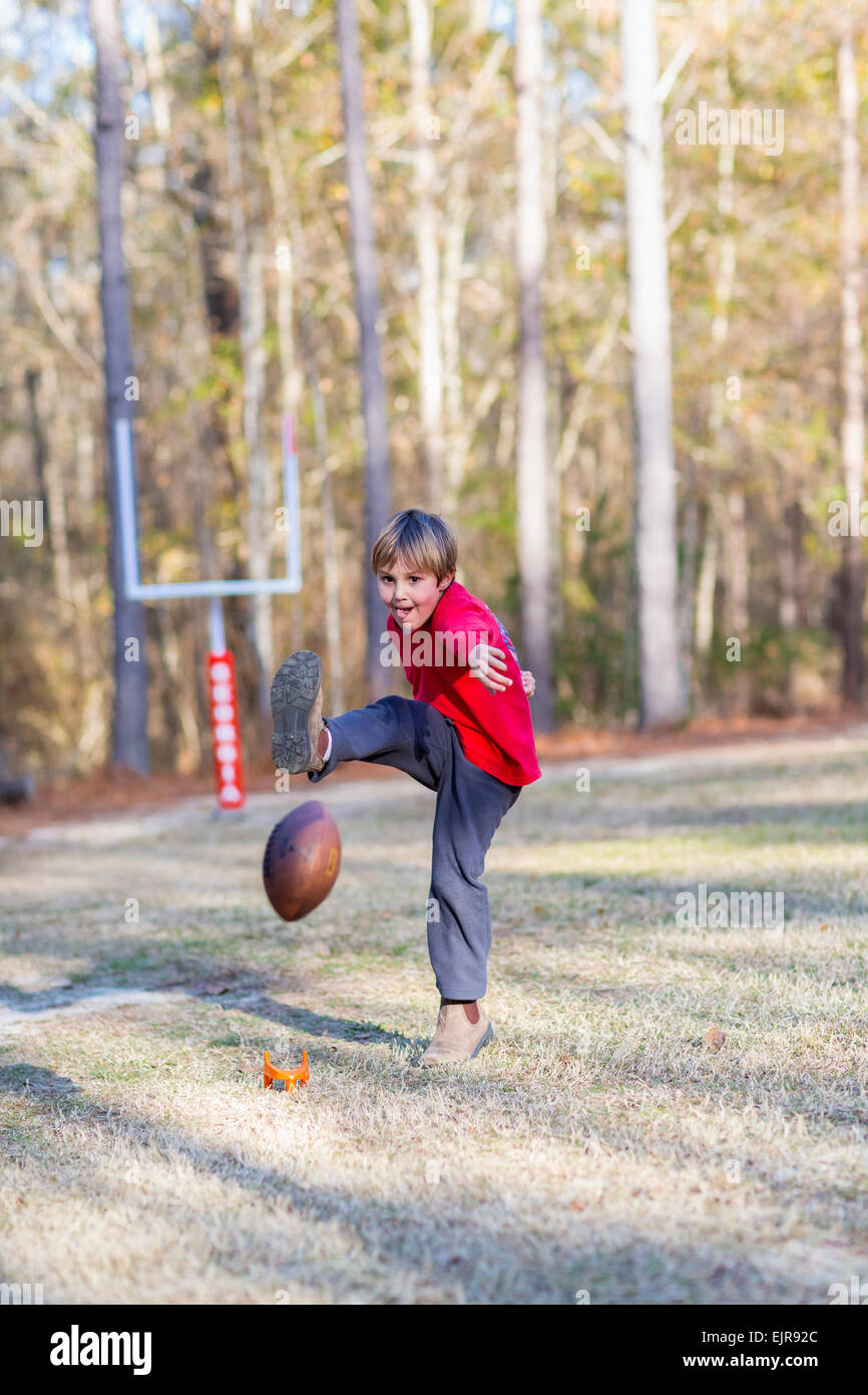 Caucasian boy kicking football in field Stock Photo