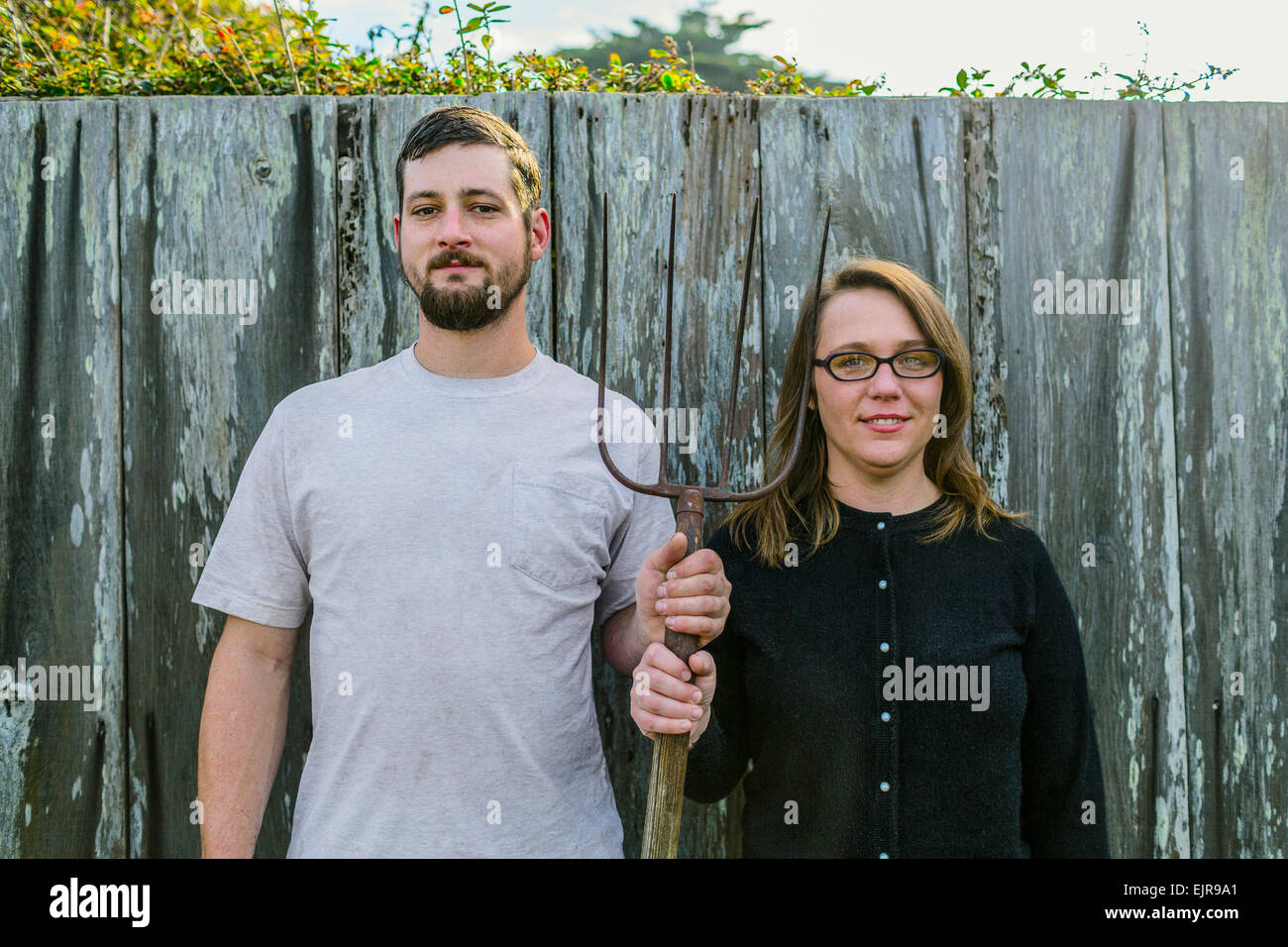 Caucasian couple holding pitchfork near fence Stock Photo