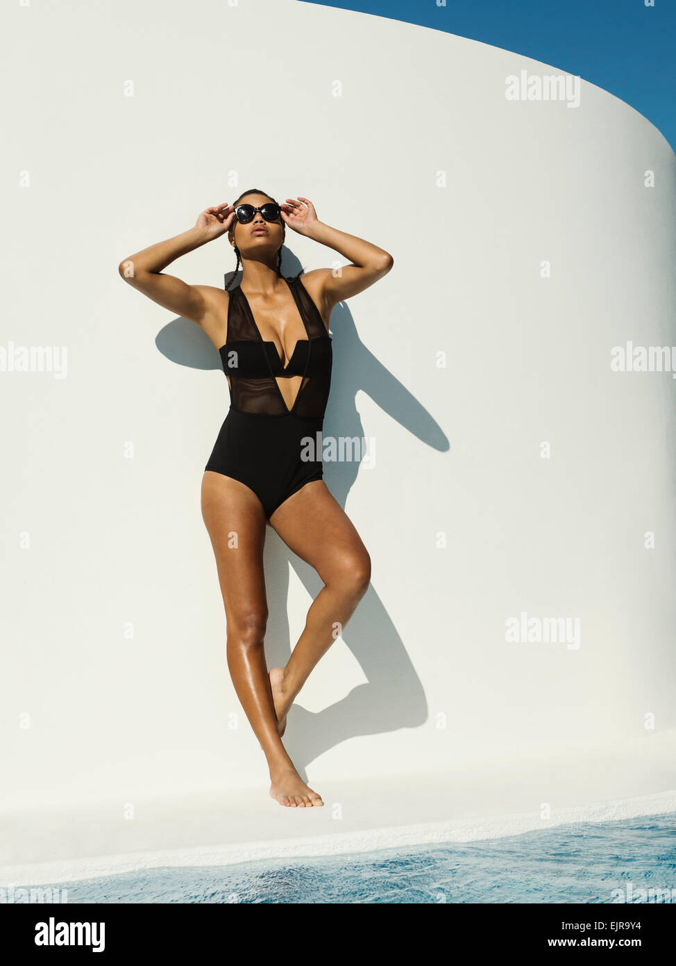 Mixed race woman in swimsuit wearing sunglasses near swimming pool Stock Photo