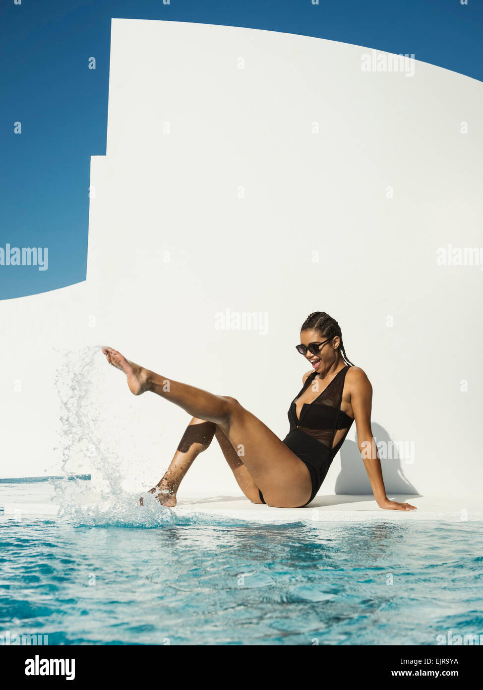 Mixed race woman in swimsuit splashing in swimming pool Stock Photo