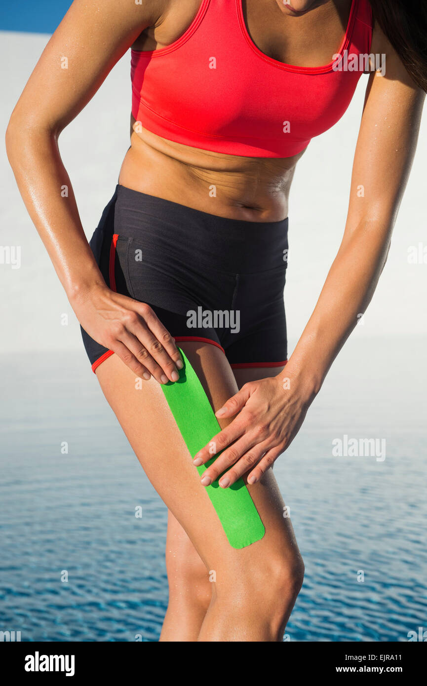 Caucasian athlete taping thigh near swimming pool Stock Photo