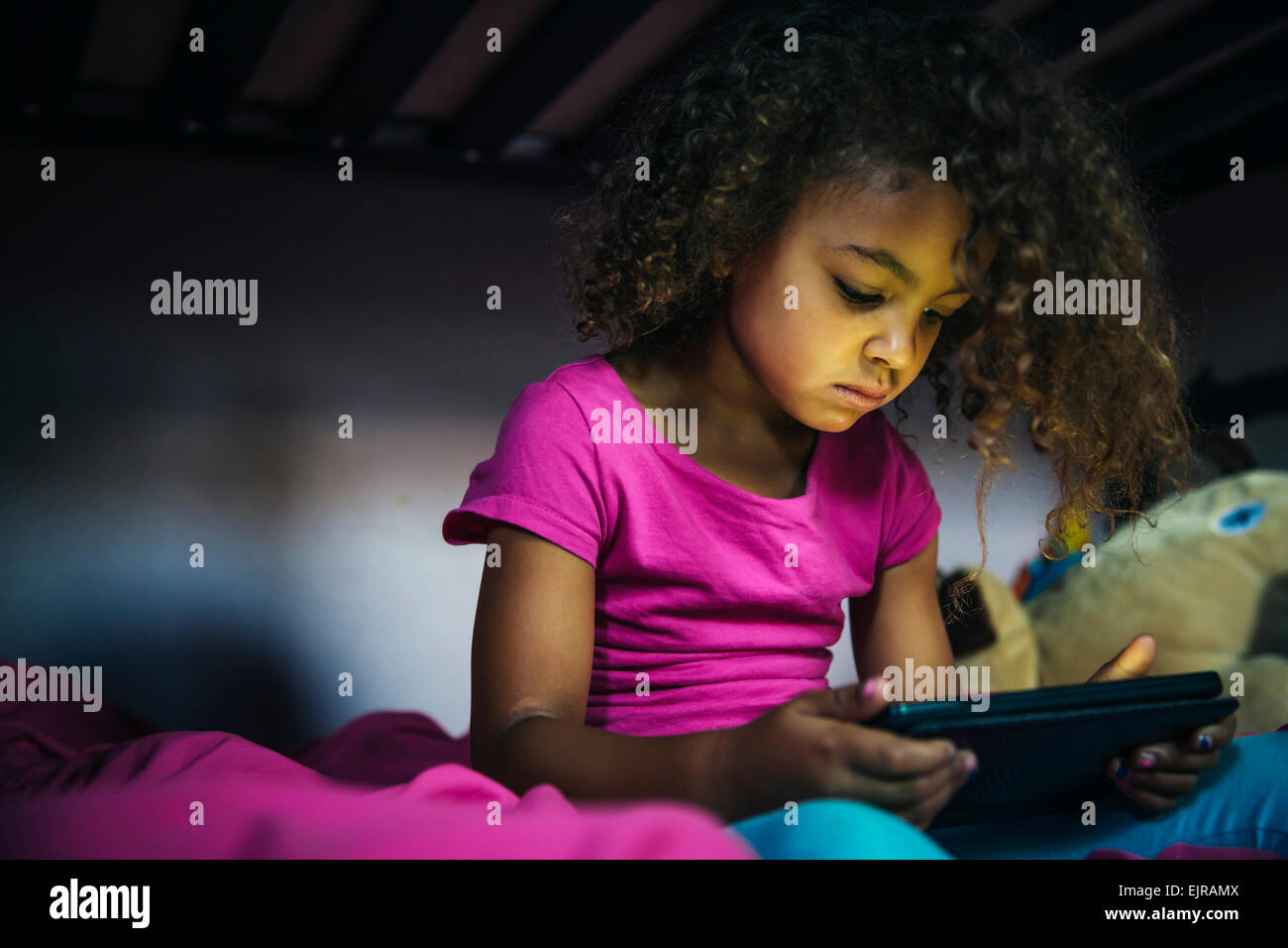 Mixed race girl using digital tablet on bed Stock Photo