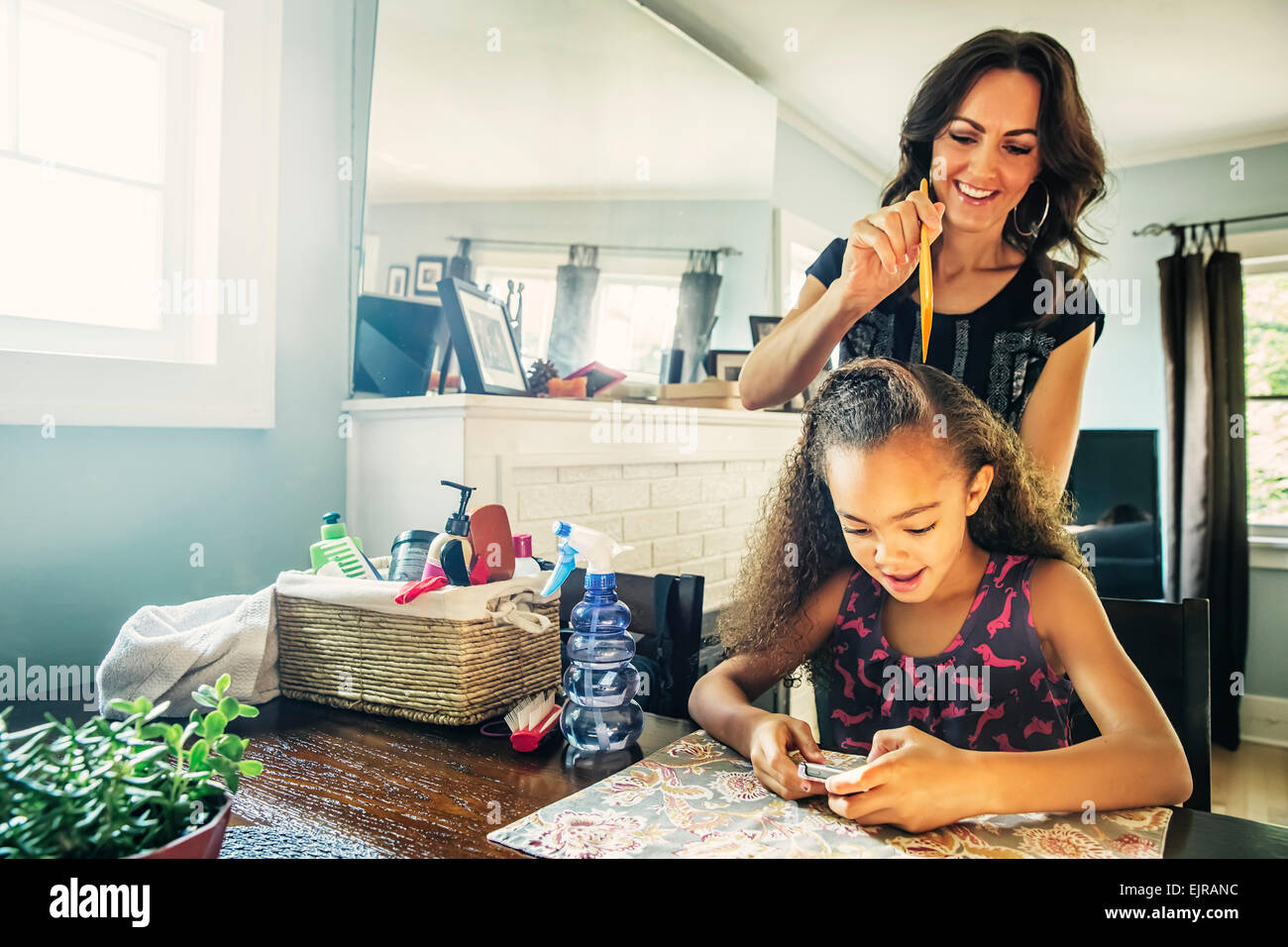 Mother combing hair of daughter at kitchen table Stock Photo