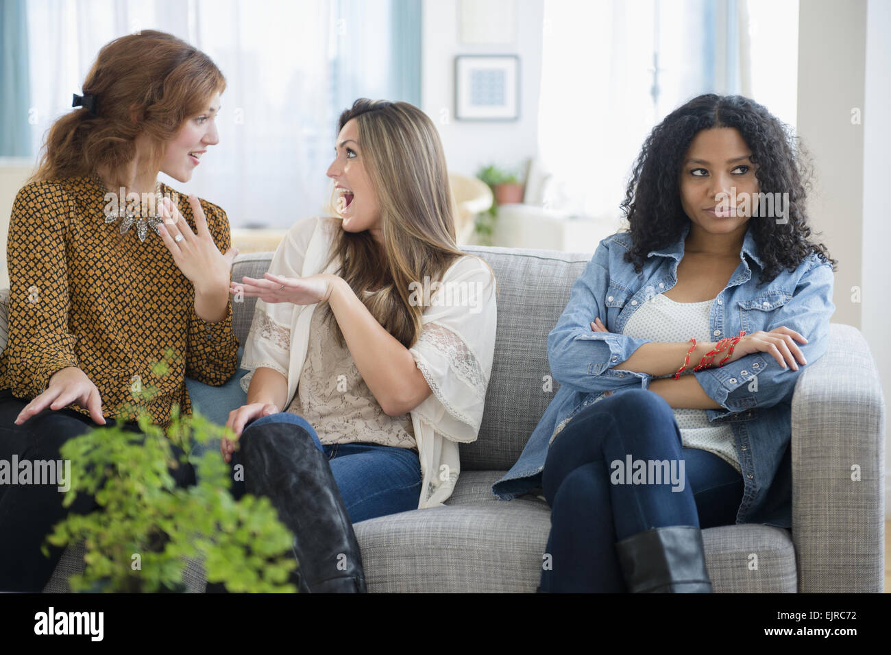 Chatting women ignoring upset friend on sofa Stock Photo