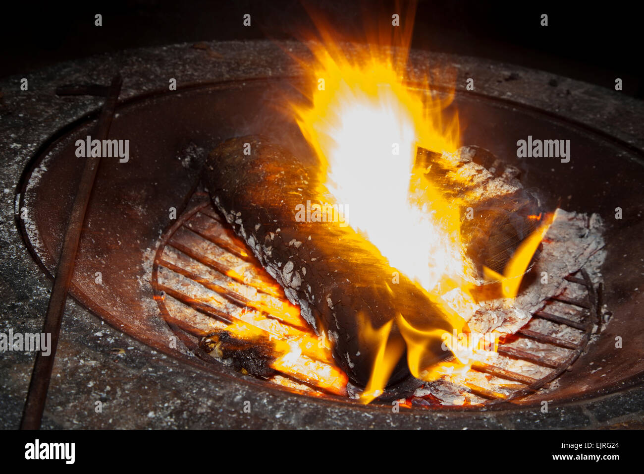 A fire glows brightly in a firepit with a poker resting on the side.  Ash and embers are visible. Stock Photo