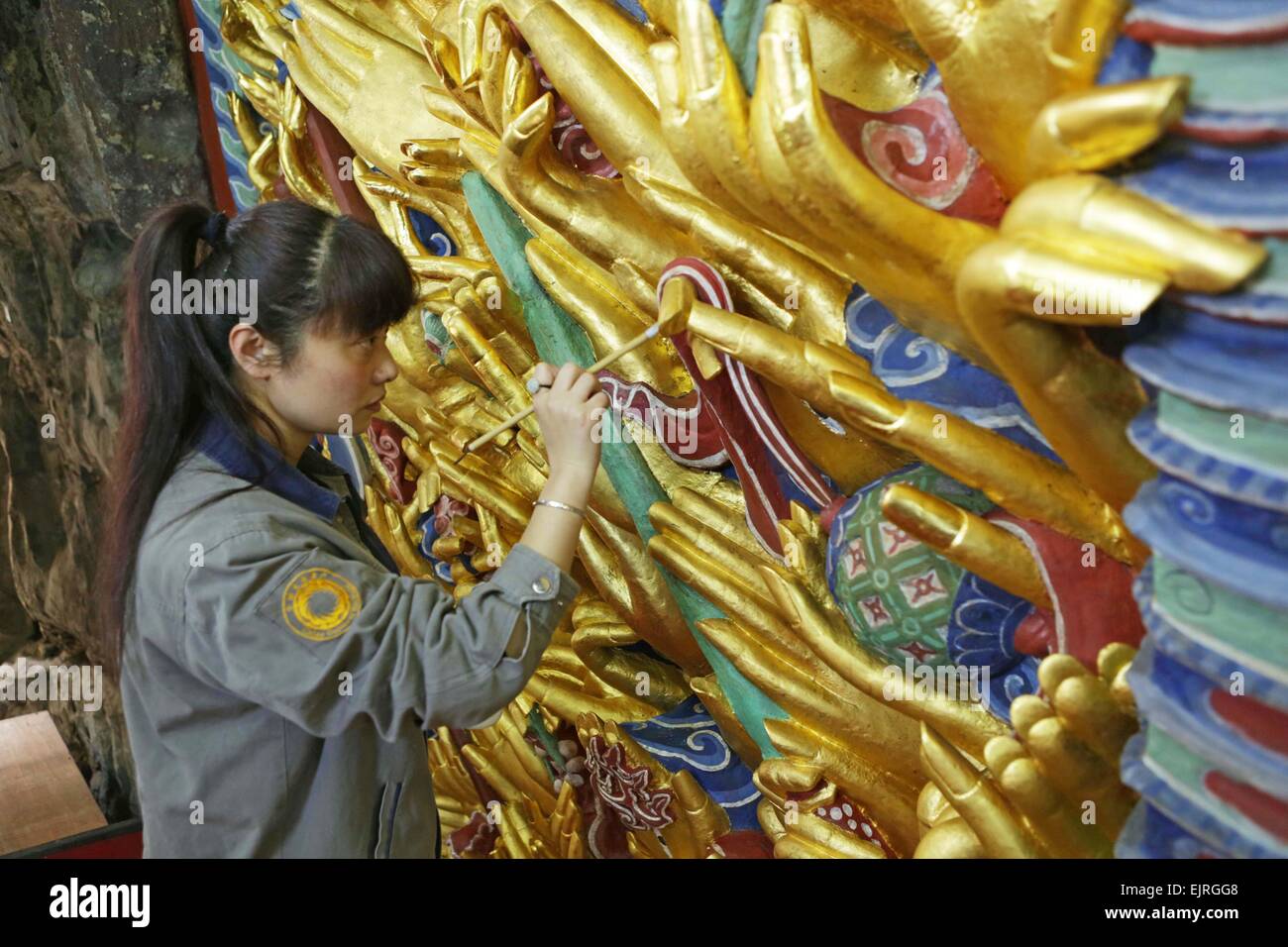 Chongqing, China. 31st Mar, 2015. A worker restores a sculpture of Qianshou Guanyin (bodhisattva with a thousand hands) on Mount Baoding in Dazu District in the municipality of Chongqing, southwest China, March 31, 2015. The sculpture with gold foil, carved in the cave with 7.7 meters high and 12.5 meters wide, could date back to Southern Song Dynasty (1127 to 1279). The restoration work has entered the final phase and is supposed to be finished in June this year, after which the sculpture will be reopened to public. © Luo Guojia/Xinhua/Alamy Live News Stock Photo
