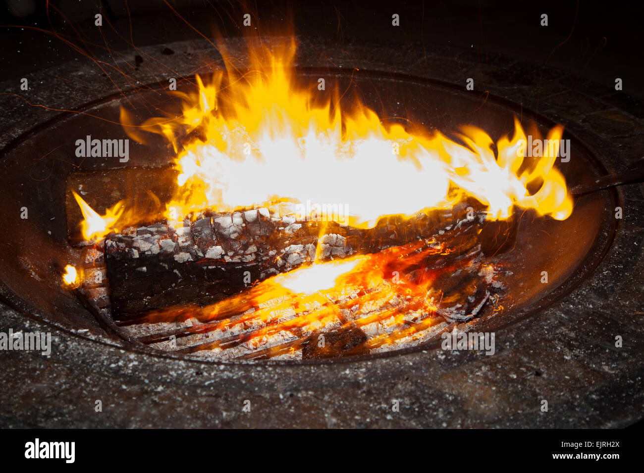 A fire glows brightly in a firepit. Ashes and embers are visible. Stock Photo