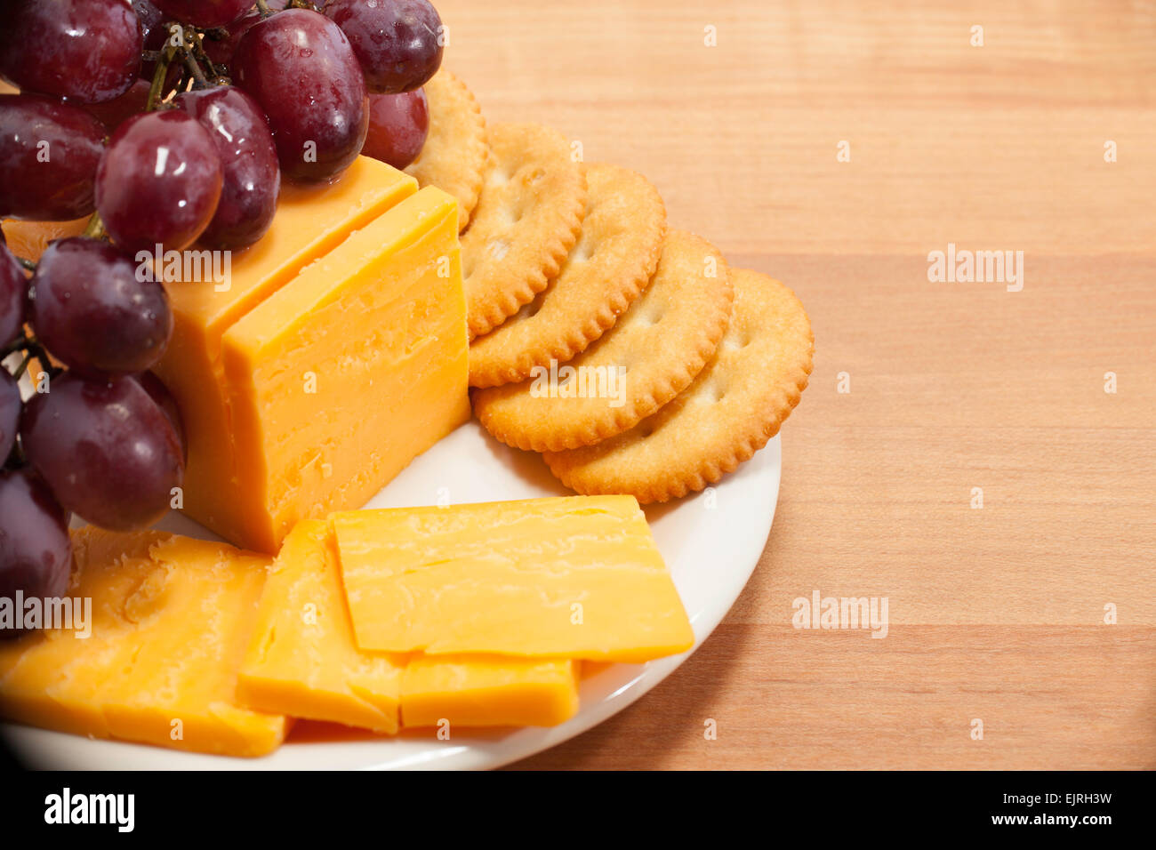 Cheddar cheese, round crackers, and red grapes are arranged on a small