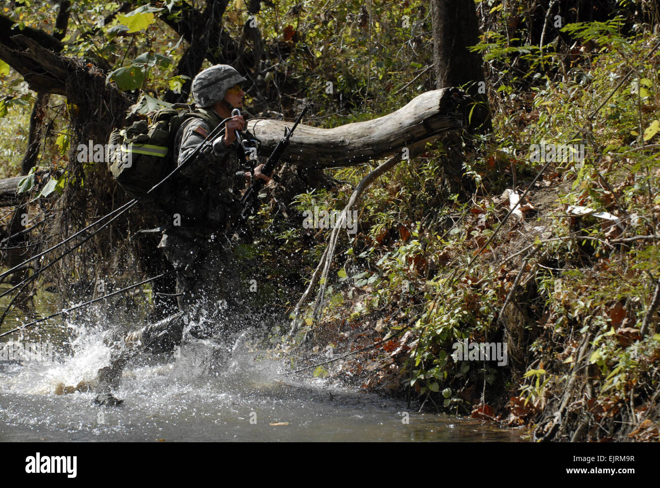 An Indiana University ROTC cadet carries ropes across a creek bed ...