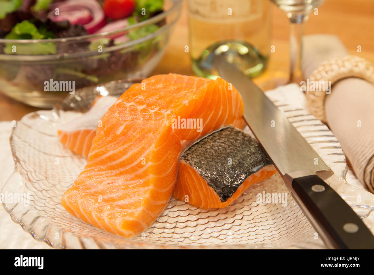 Two pieces of fresh salmon sit atop a plate ready to be cooked.  A sharp knife rests on the side of the plate. Stock Photo