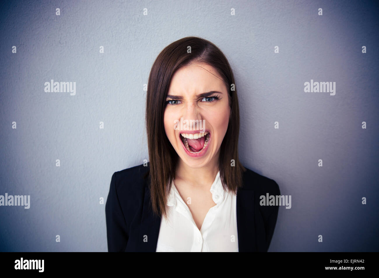 Angry businesswoman shouting over gray background. Looking at camera Stock Photo