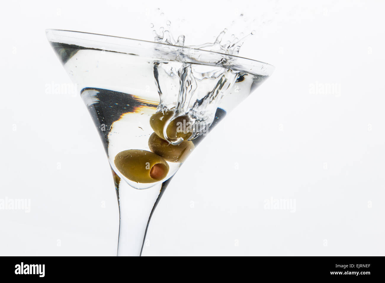 A martini glass on a white background; the water ripples and splashed as a green spanish olive with pimento is dropped into the Stock Photo