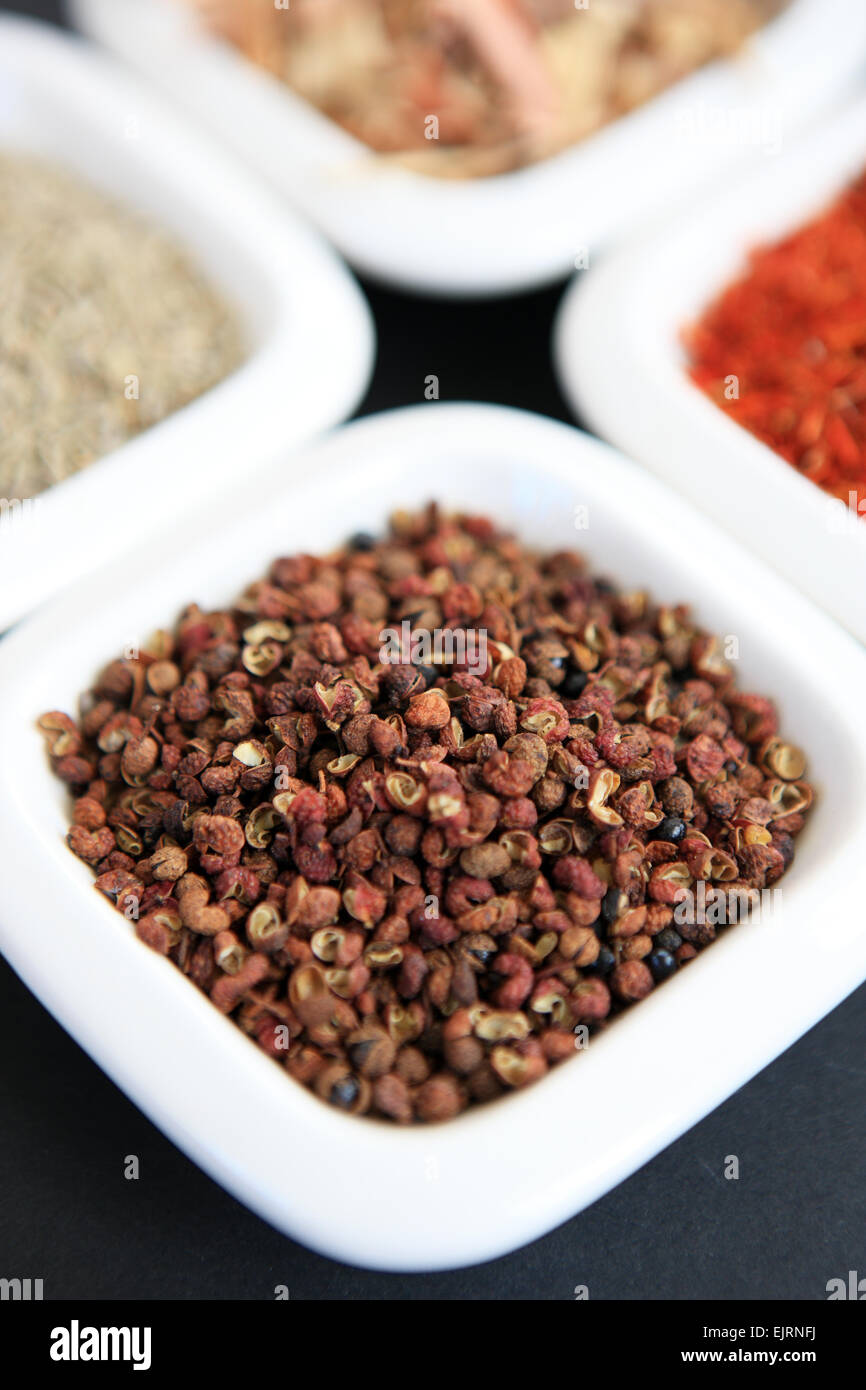 Szechuan peppercorns with, clockwise from the peppercorns, cumin seeds, lemongrass and saffron in white dishes Stock Photo