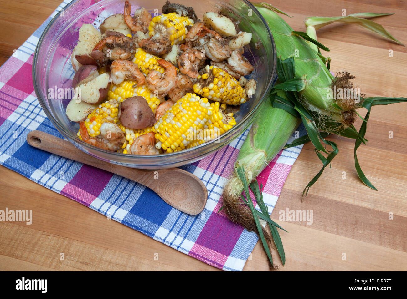 A glass bowl is filled with corn on the cob, red potatoes, and shrimp - a classic shrimp boil. Stock Photo