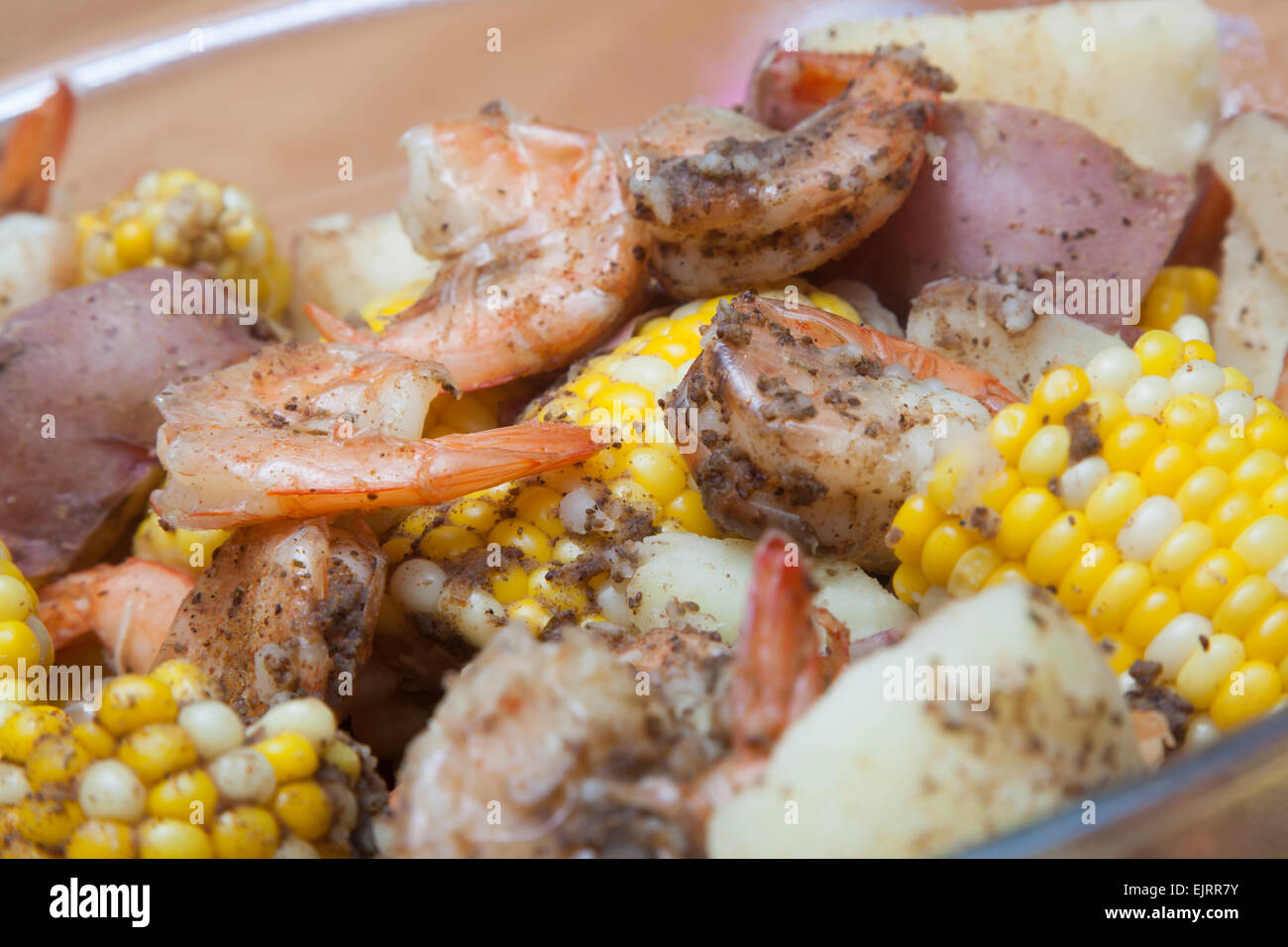 A glass bowl is filled with corn on the cob, red potatoes, and shrimp - a classic shrimp boil Stock Photo