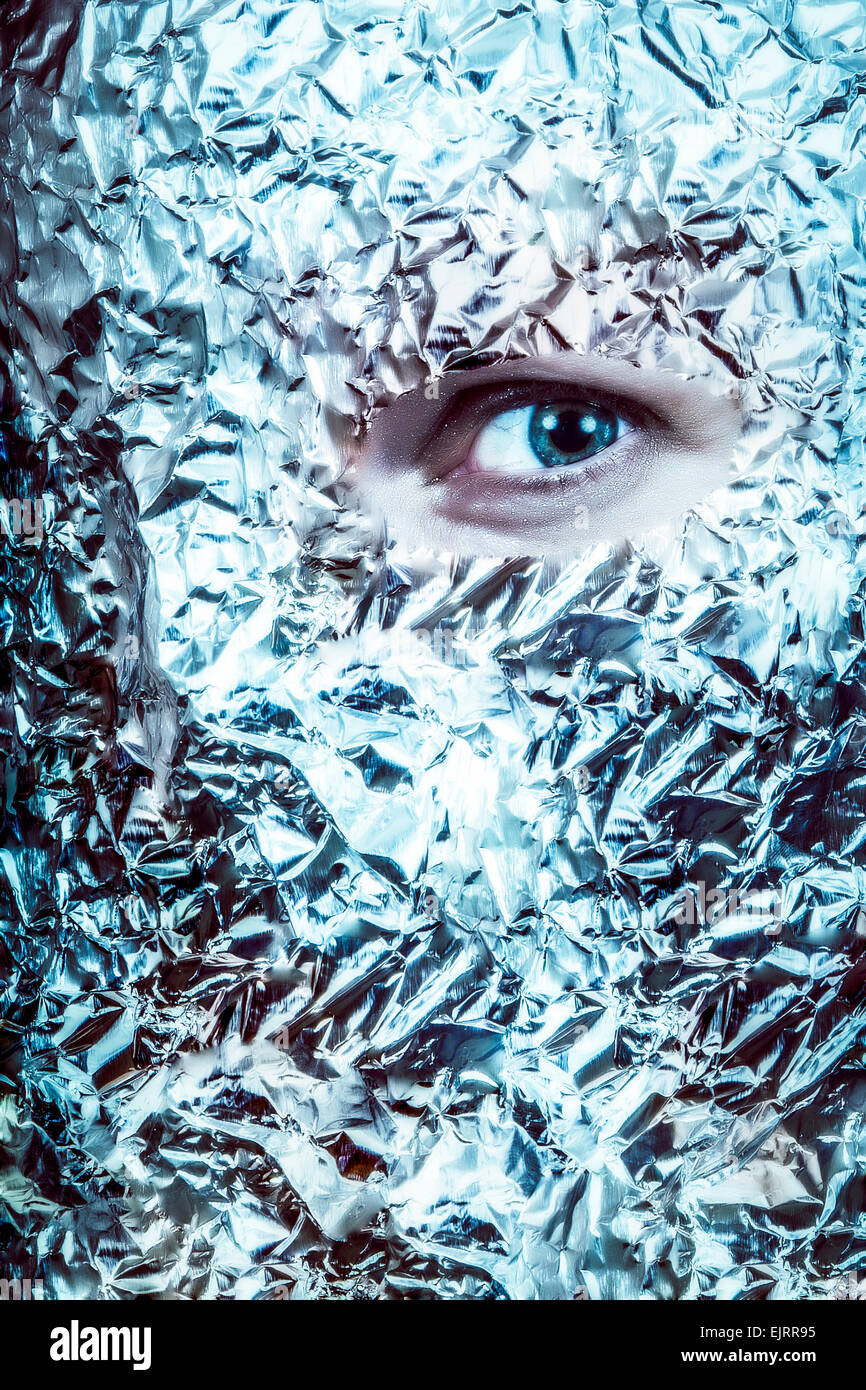 An eye peeks out of  a mask of tin foil.  Looks frightening and surreal.  Split color tone Stock Photo