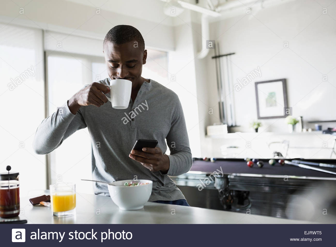 Man sipping morning coffee and texting in kitchen Stock Photo
