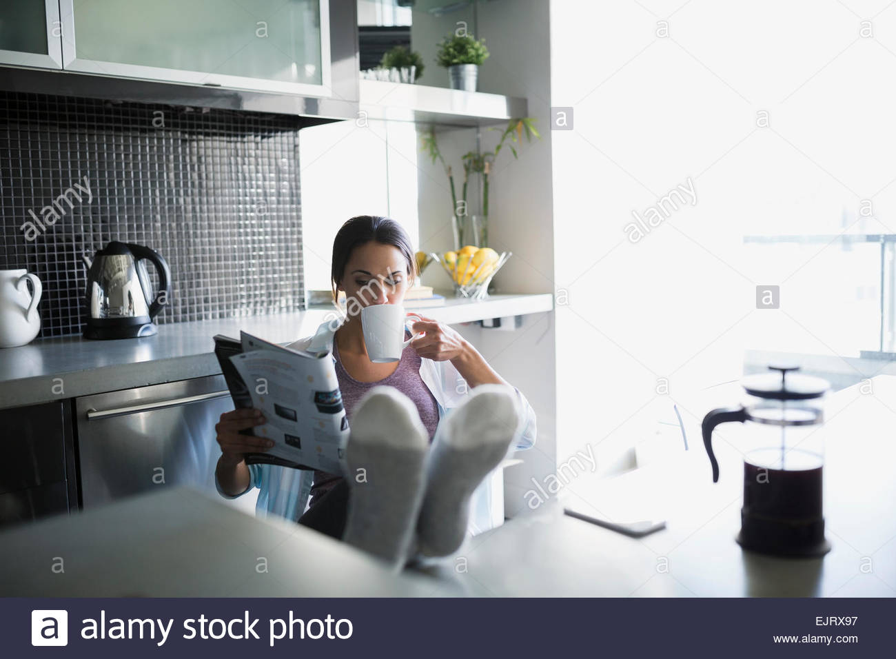 Woman drinking coffee reading magazine with feet up Stock Photo