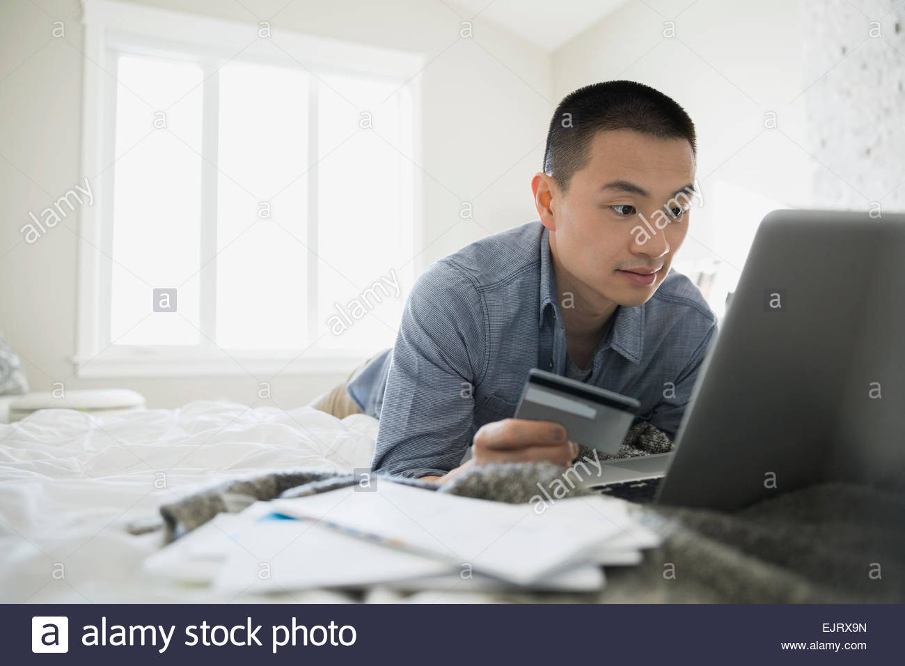 Man with credit card and laptop on bed Stock Photo Alamy