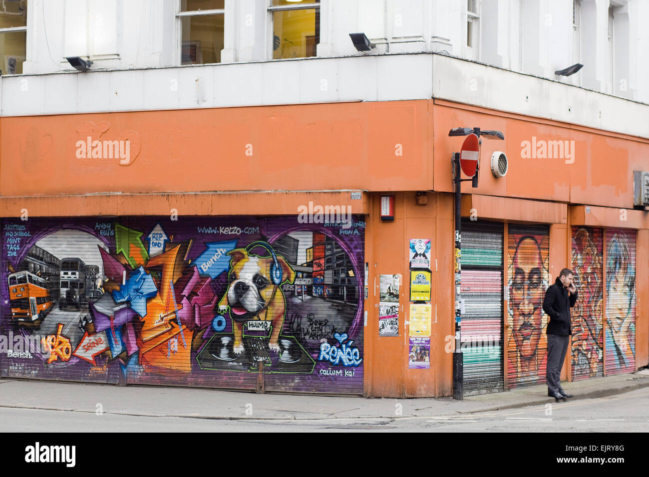 Man standing using his phone on the corner by a Graffiti covered shop front Stock Photo