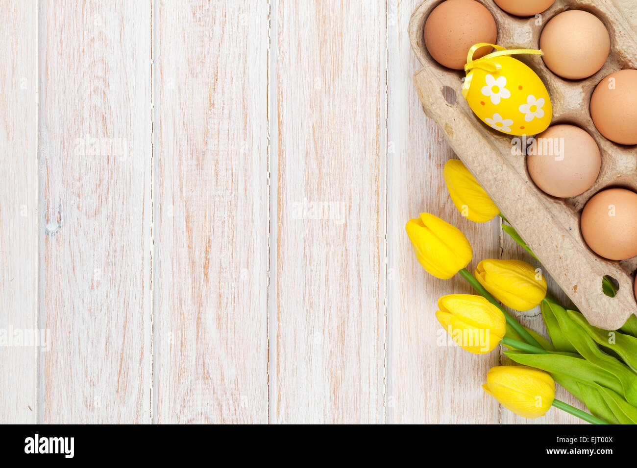 Easter background with eggs and yellow tulips over white wood. Top view ...