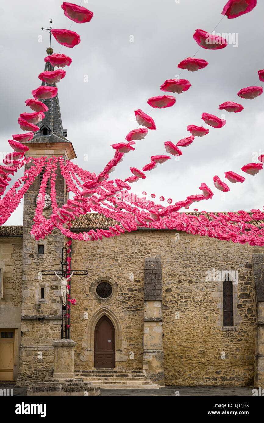Colourful display of pink and white paper flowers draped across a town square from the church spire in Villefranche de Longchat. Stock Photo