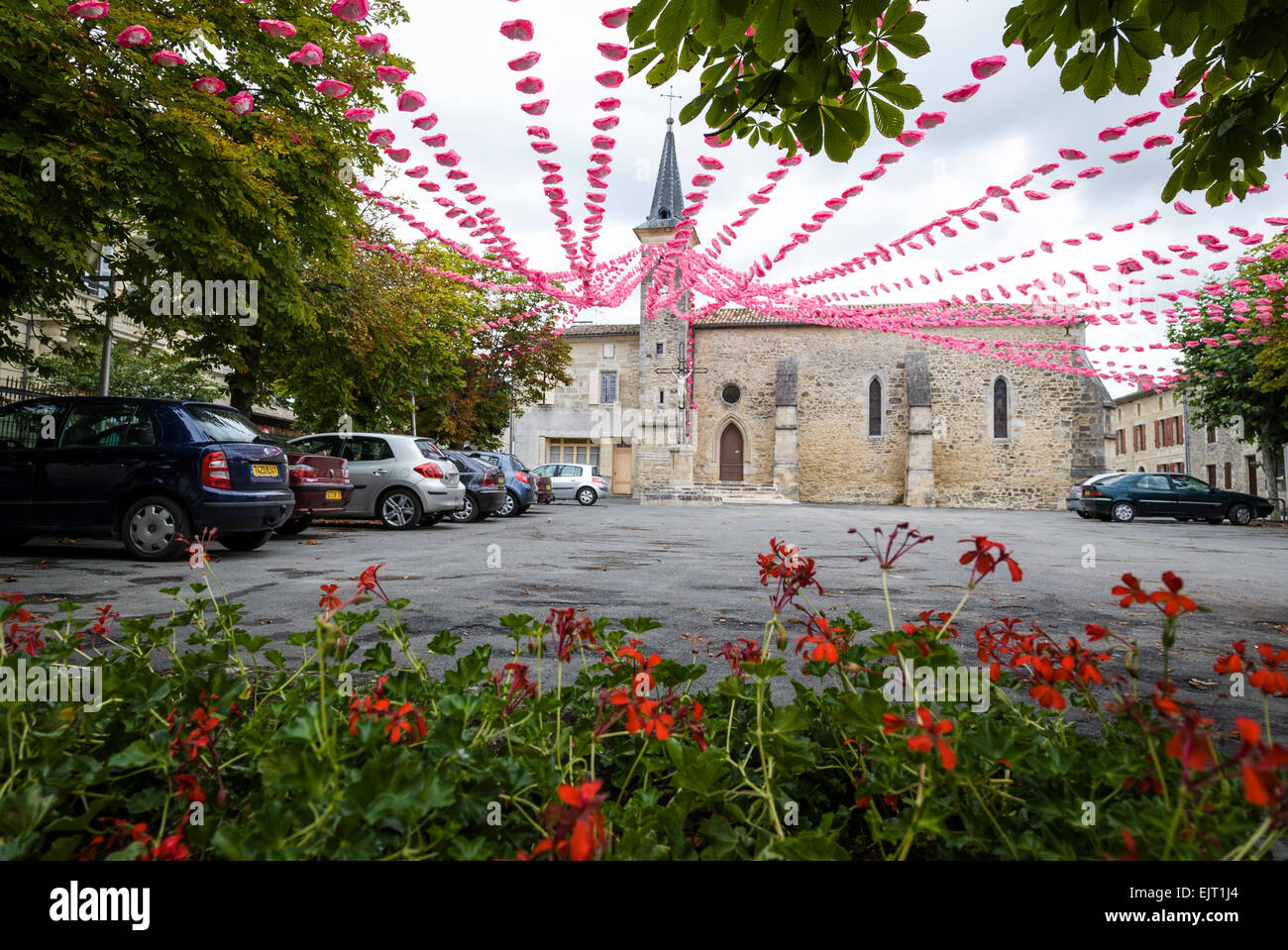 Colourful display of pink and white paper flowers draped across a town square  in Villefranche de Longchat, France. Stock Photo