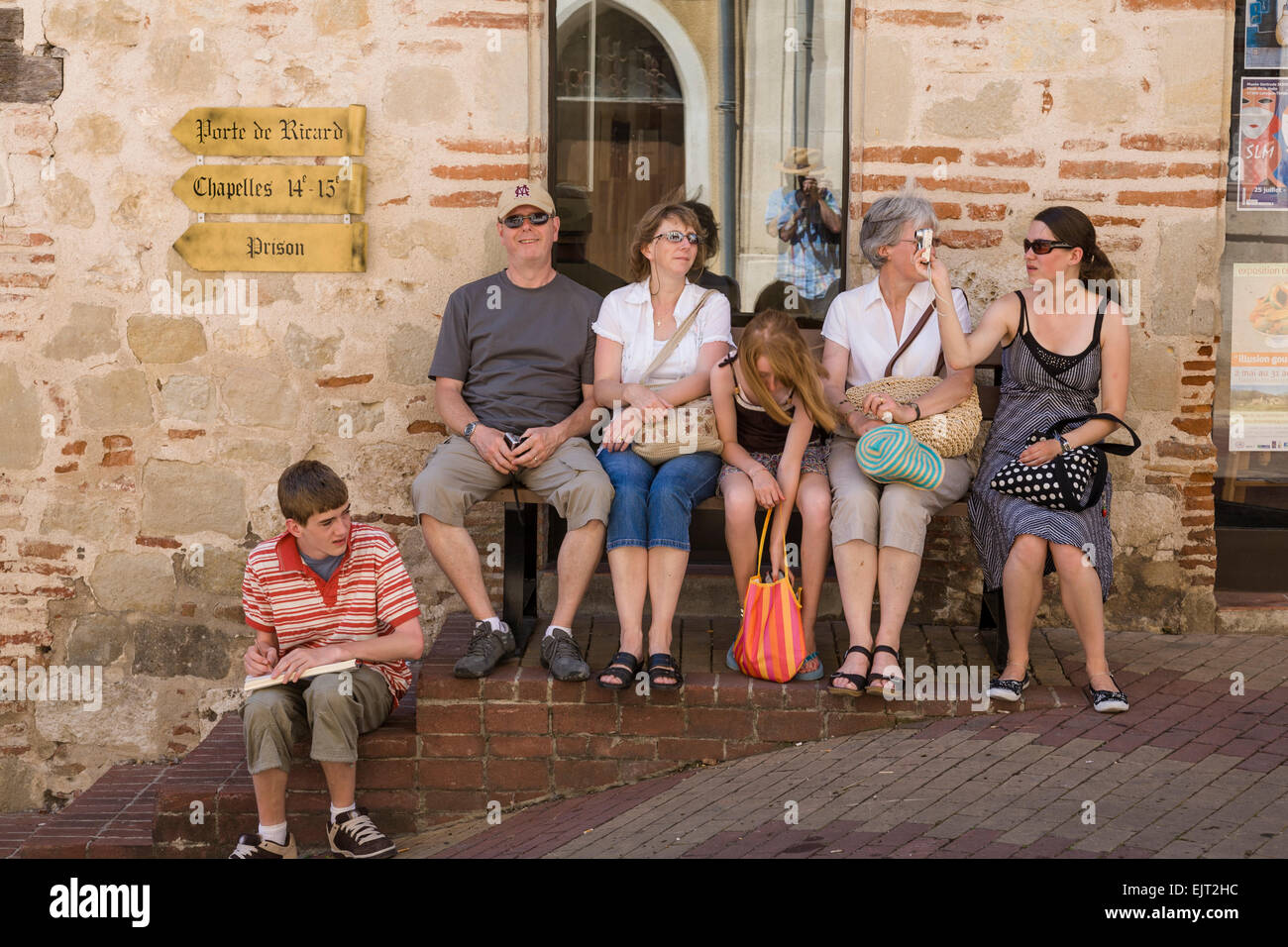 Family group sit and relax on steps and a wooden bench in Penne d'Agenais Stock Photo