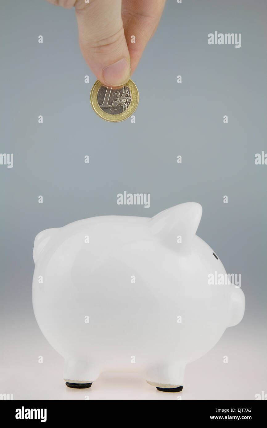 White Piggy Bank with a Hand above about to drop a One Euro Coin into the slot, Stock Photo
