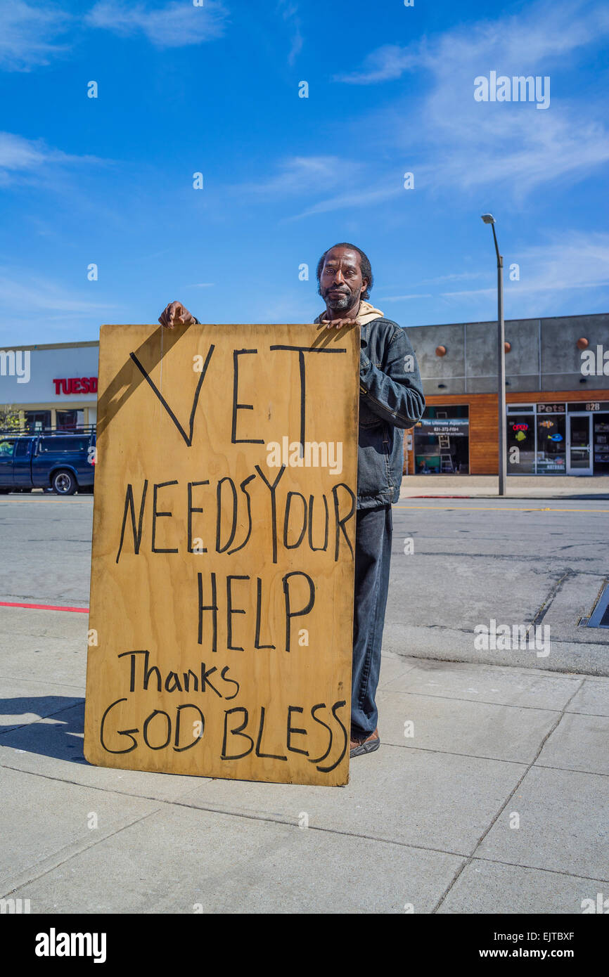 An African-American veteran of the Iraq war holds up an over-sized plywood sign outside a coffee drive through begging for money Stock Photo
