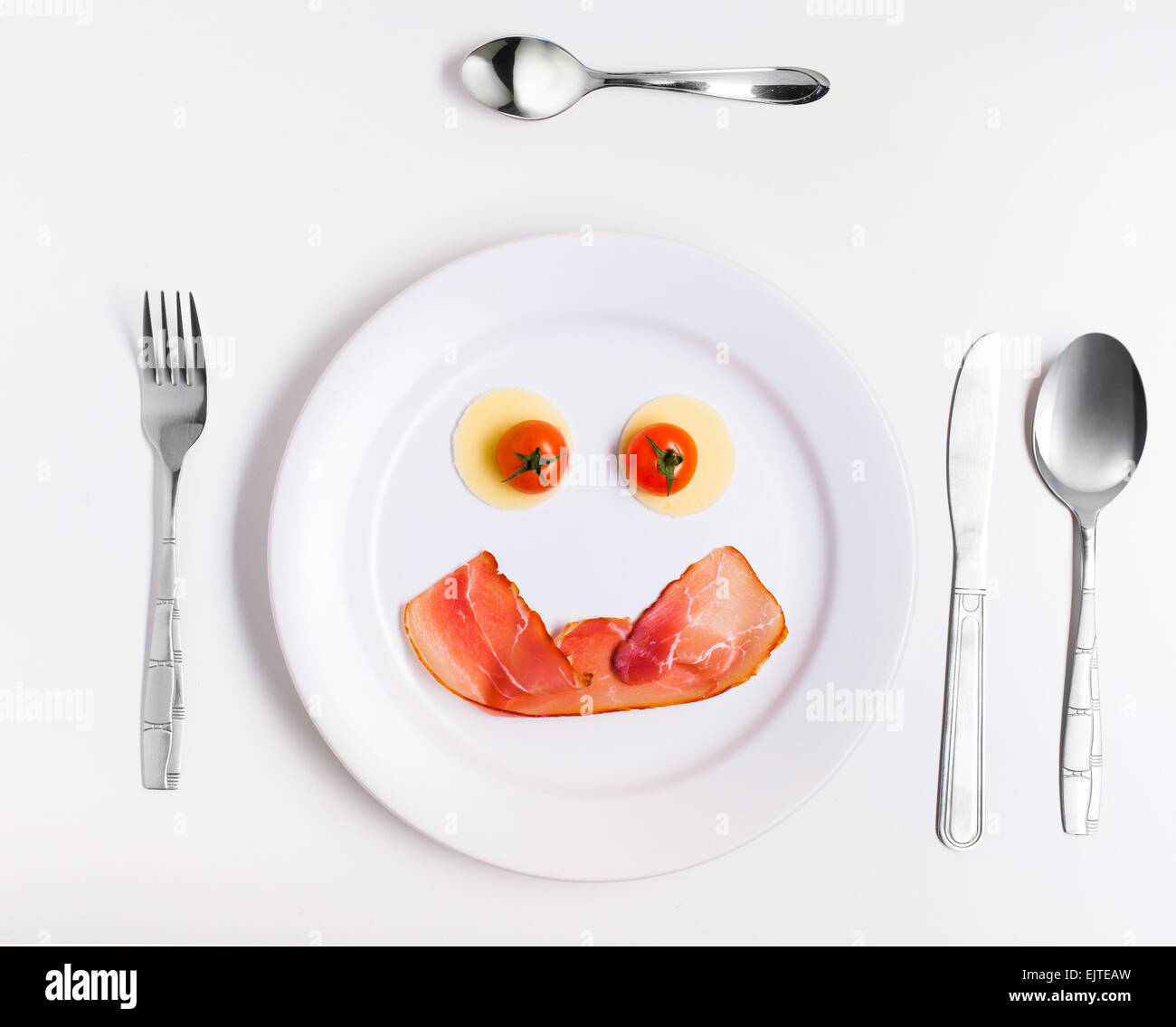 smiley face emoticon made from ham, cheese and tomatoes on a plate with cutlery Stock Photo