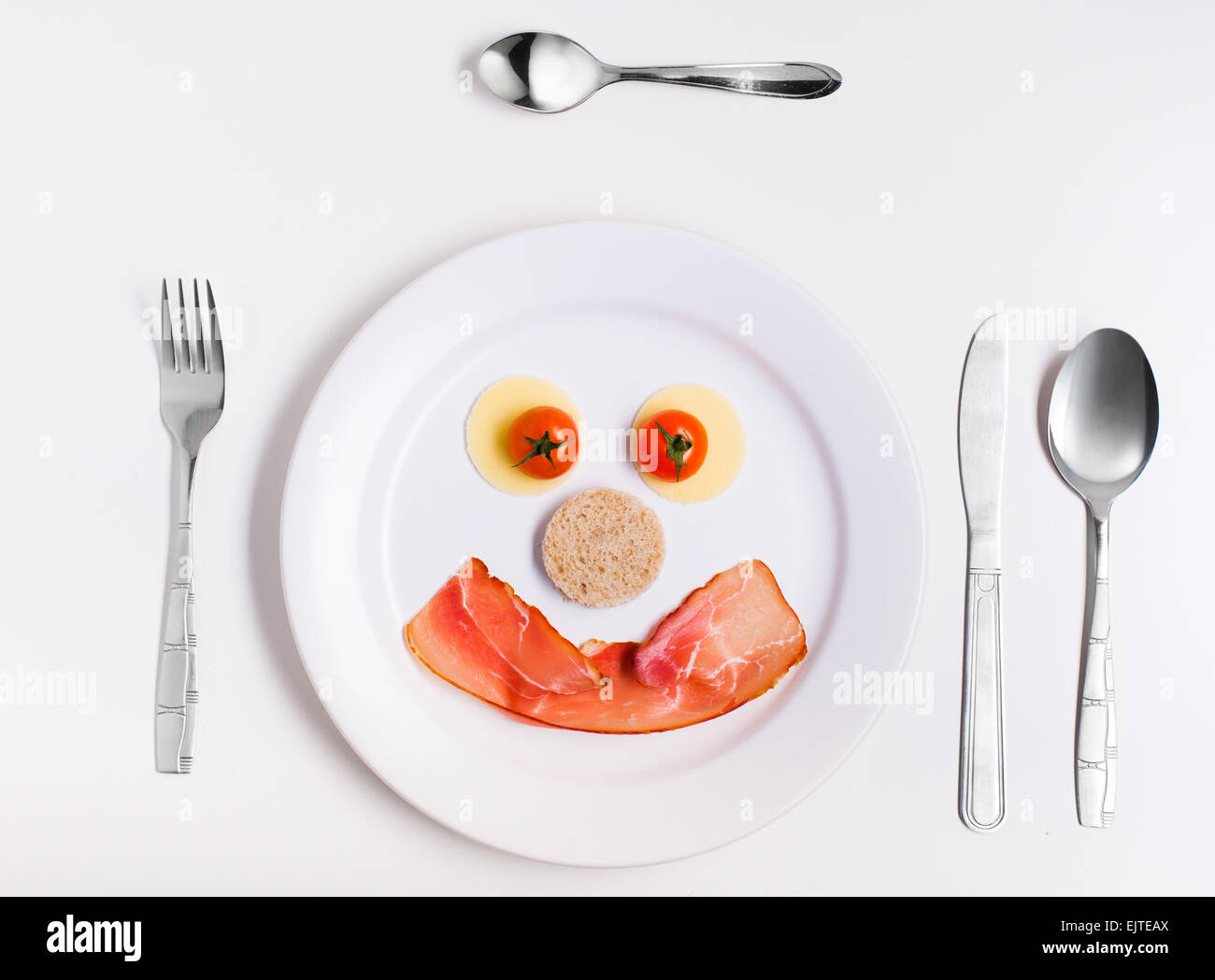 smiley face emoticon made from ham, cheese and tomatoes on a plate with cutlery Stock Photo