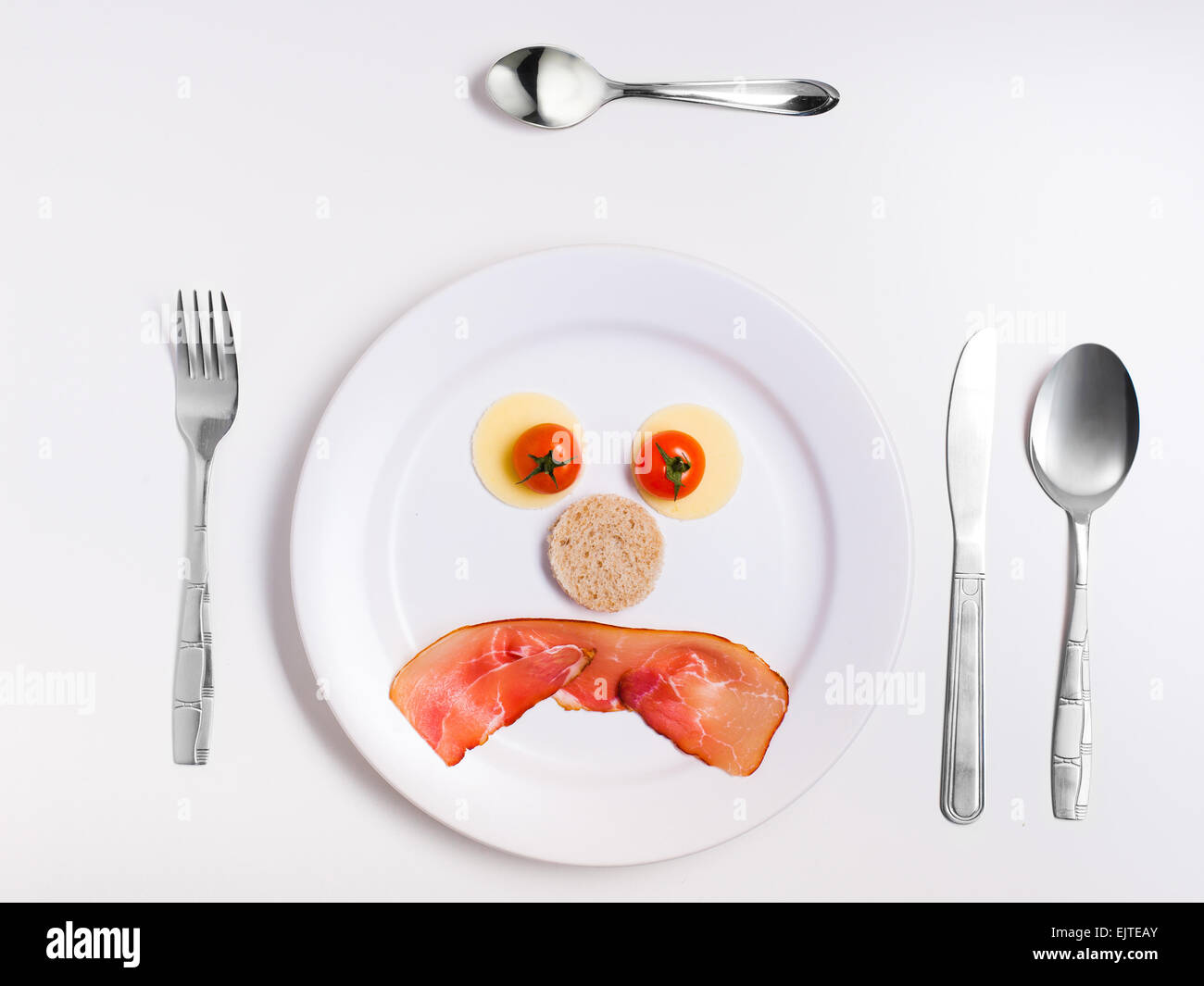 sad emoticon food, made from cheese, tomatoes, bread and ham on a plate with cutlery Stock Photo