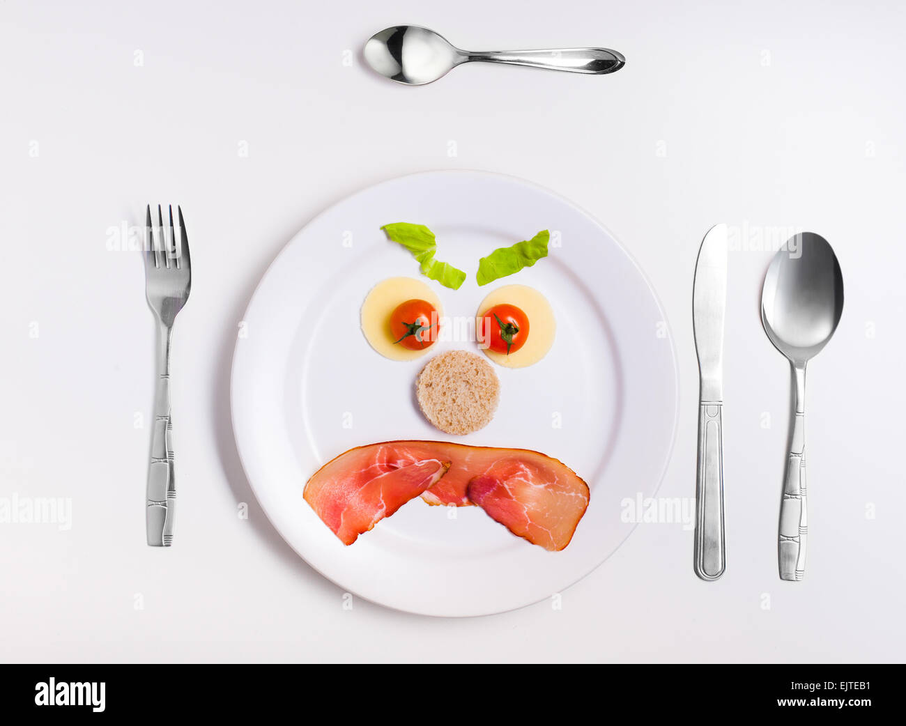 angry emoticon food, made from cheese, tomatoes, bread and ham on a plate with cutlery Stock Photo