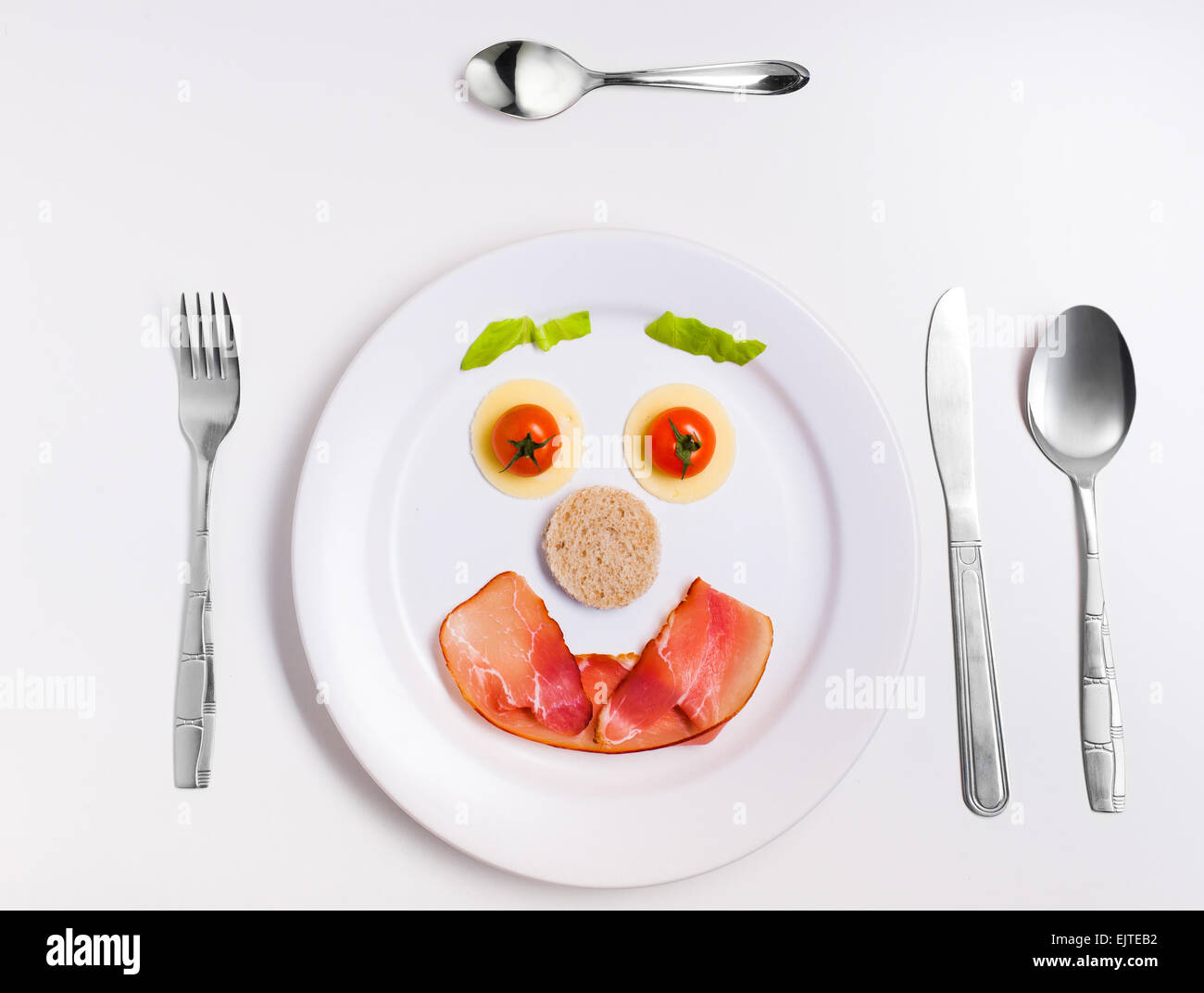 happy emoticon food, made from cheese, tomatoes, bread and ham on a plate with cutlery Stock Photo