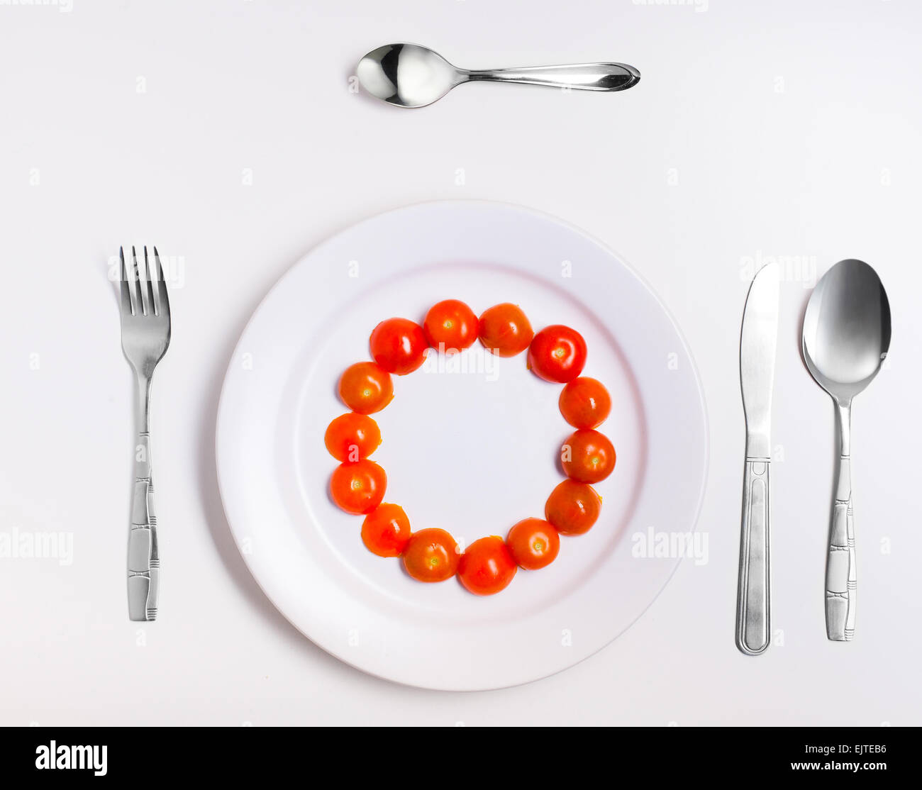tomatoes circle on a plate with cutlery on white Stock Photo