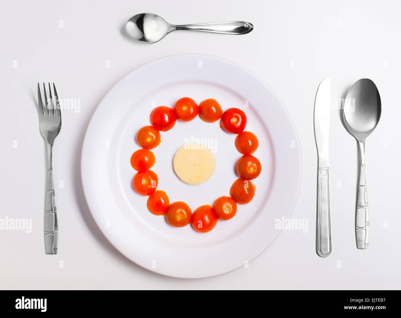tomatoes circle and cheese on a plate with cutlery on white Stock Photo