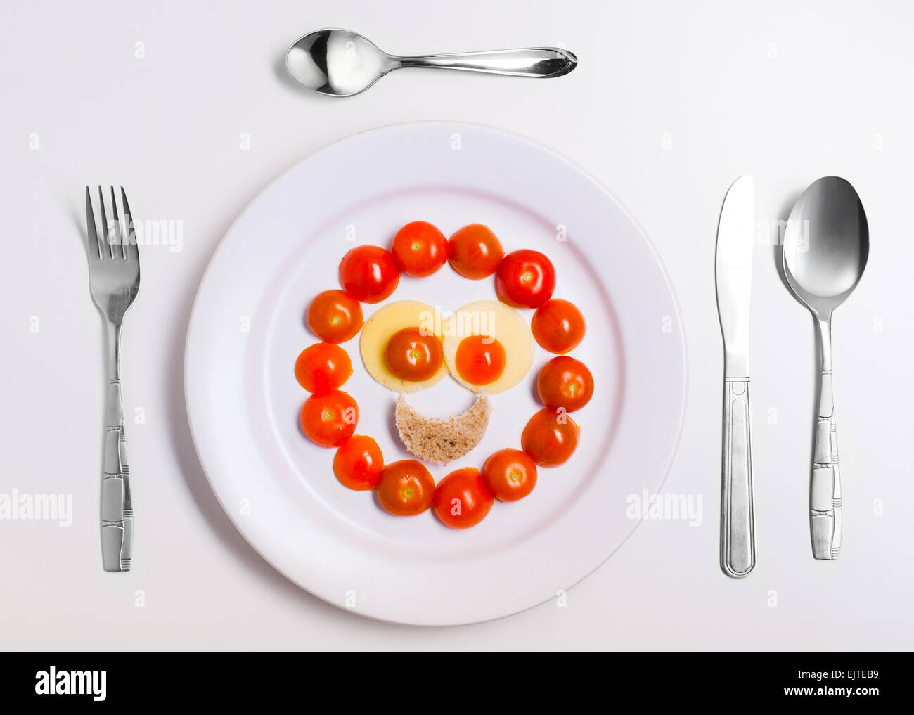 fun emoticon food, made from cheese and tomatoes, on a plate with cutlery, isolated Stock Photo