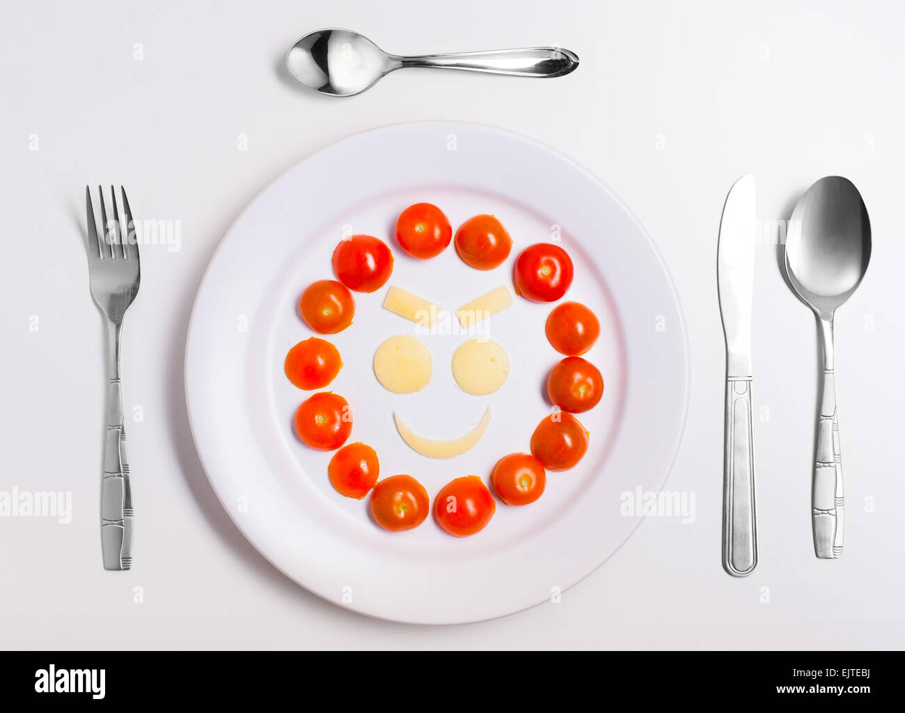 mean emoticon food, made from cheese and tomatoes, on a plate with cutlery, isolated Stock Photo