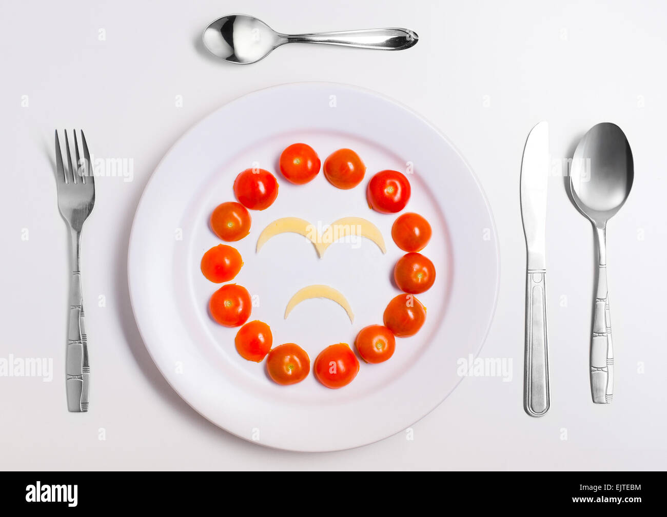 sad emoticon food, made from cheese and tomatoes, on a plate with cutlery, isolated Stock Photo