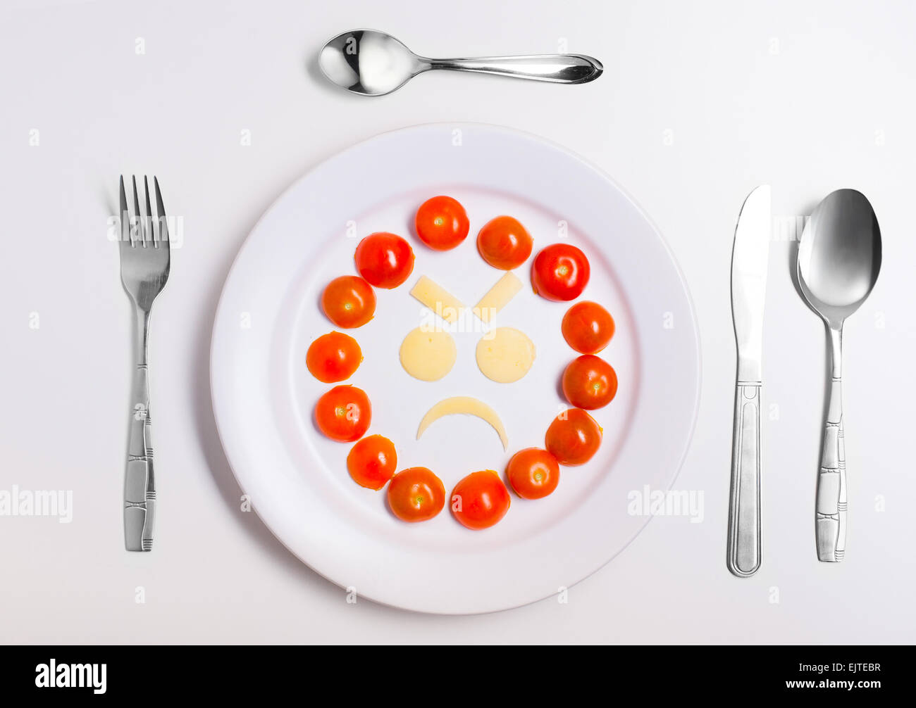 angry emoticon food, made from cheese and tomatoes, on a plate with cutlery, isolated Stock Photo