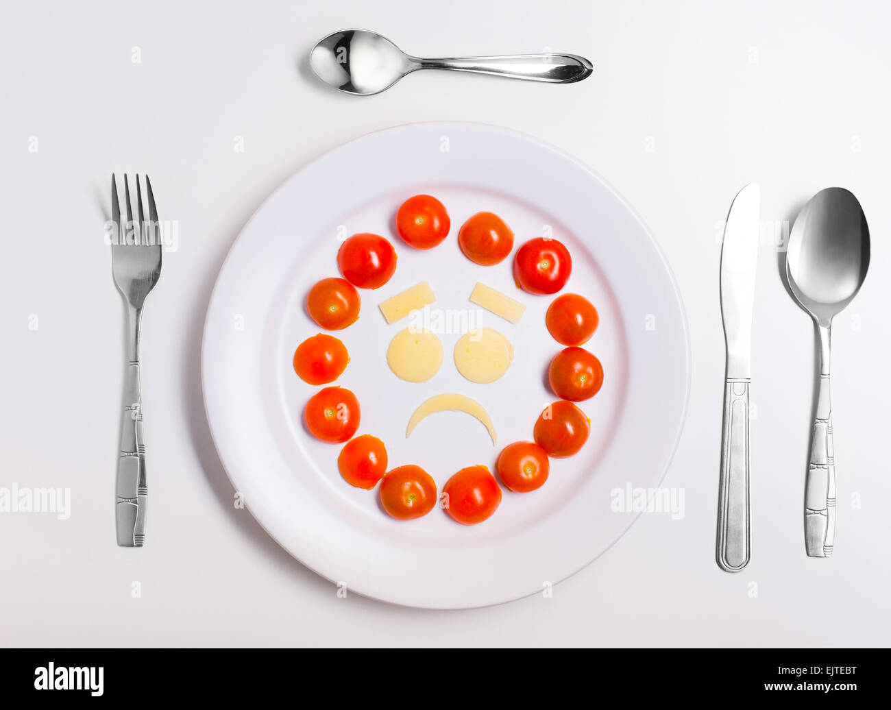 disappointed emoticon food, made from cheese and tomatoes, on a plate with cutlery, isolated Stock Photo