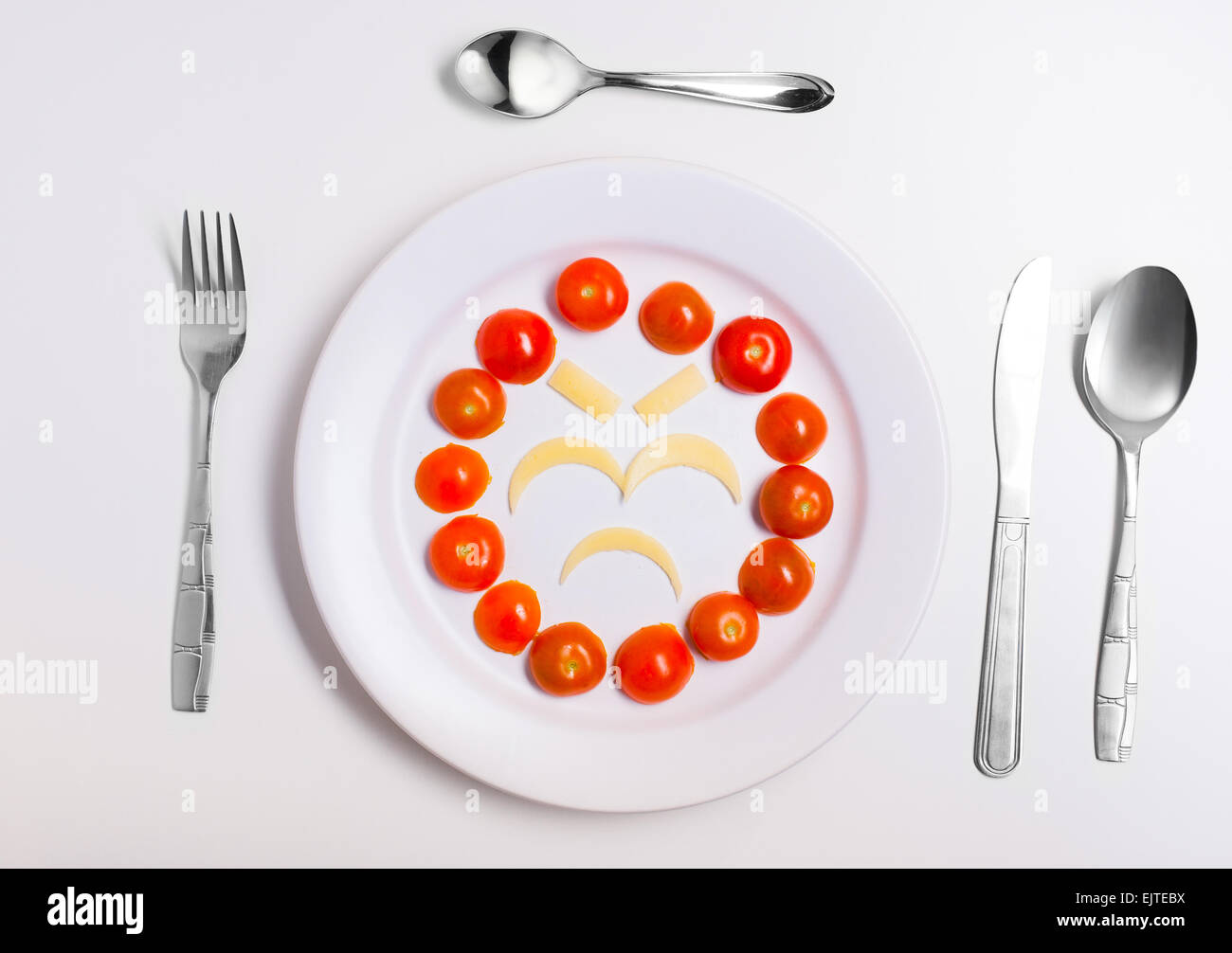 angry and disappointed emoticon food, made from cheese and tomatoes, on a plate with cutlery, isolated Stock Photo