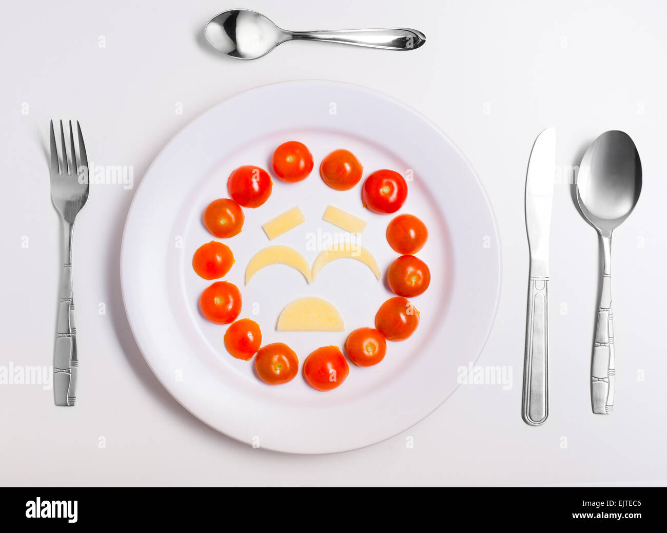 crying emoticon food, made from cheese and tomatoes, on a plate with cutlery, isolated Stock Photo
