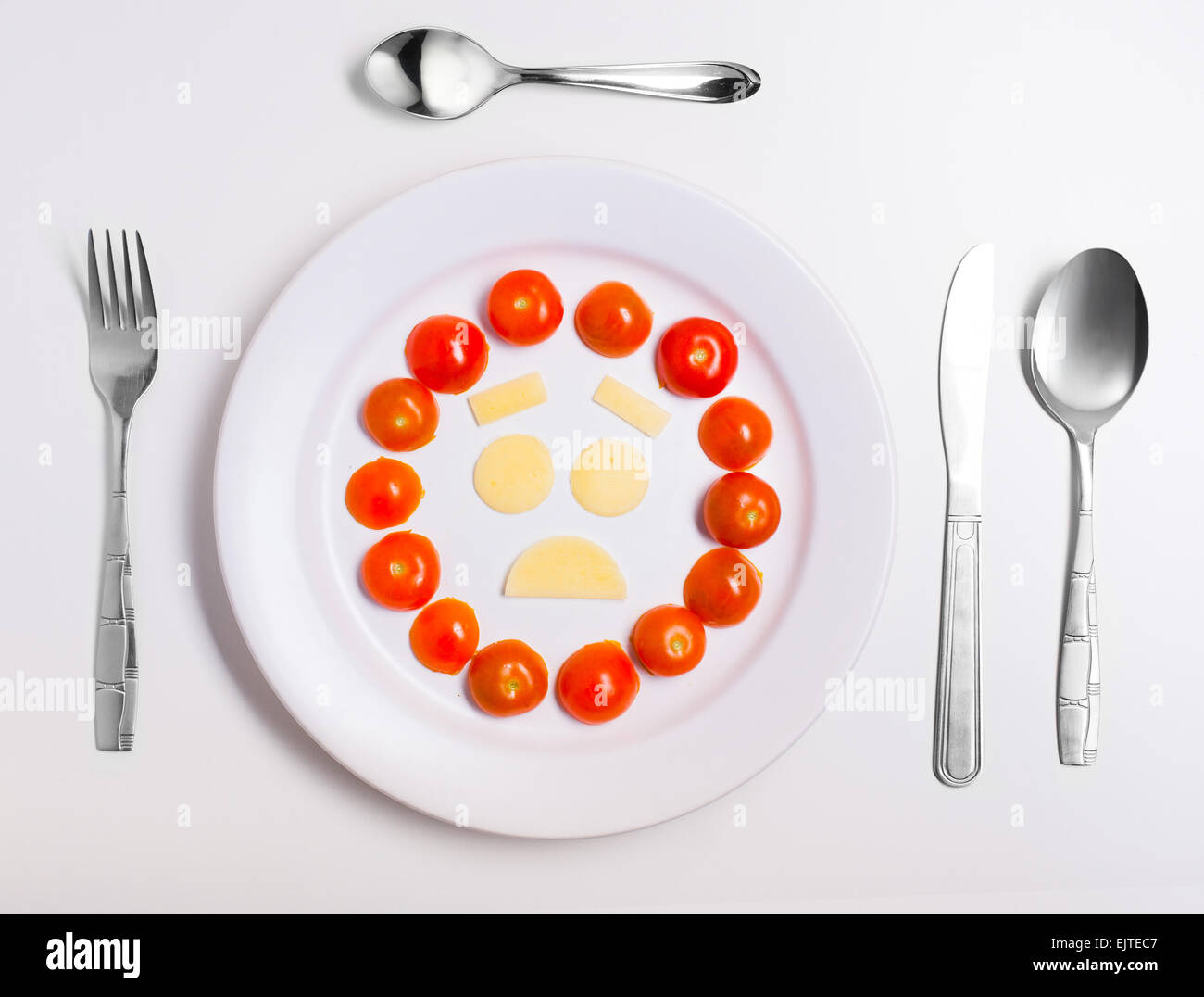 disappointed emoticon food, made from cheese and tomatoes, on a plate with cutlery, isolated Stock Photo
