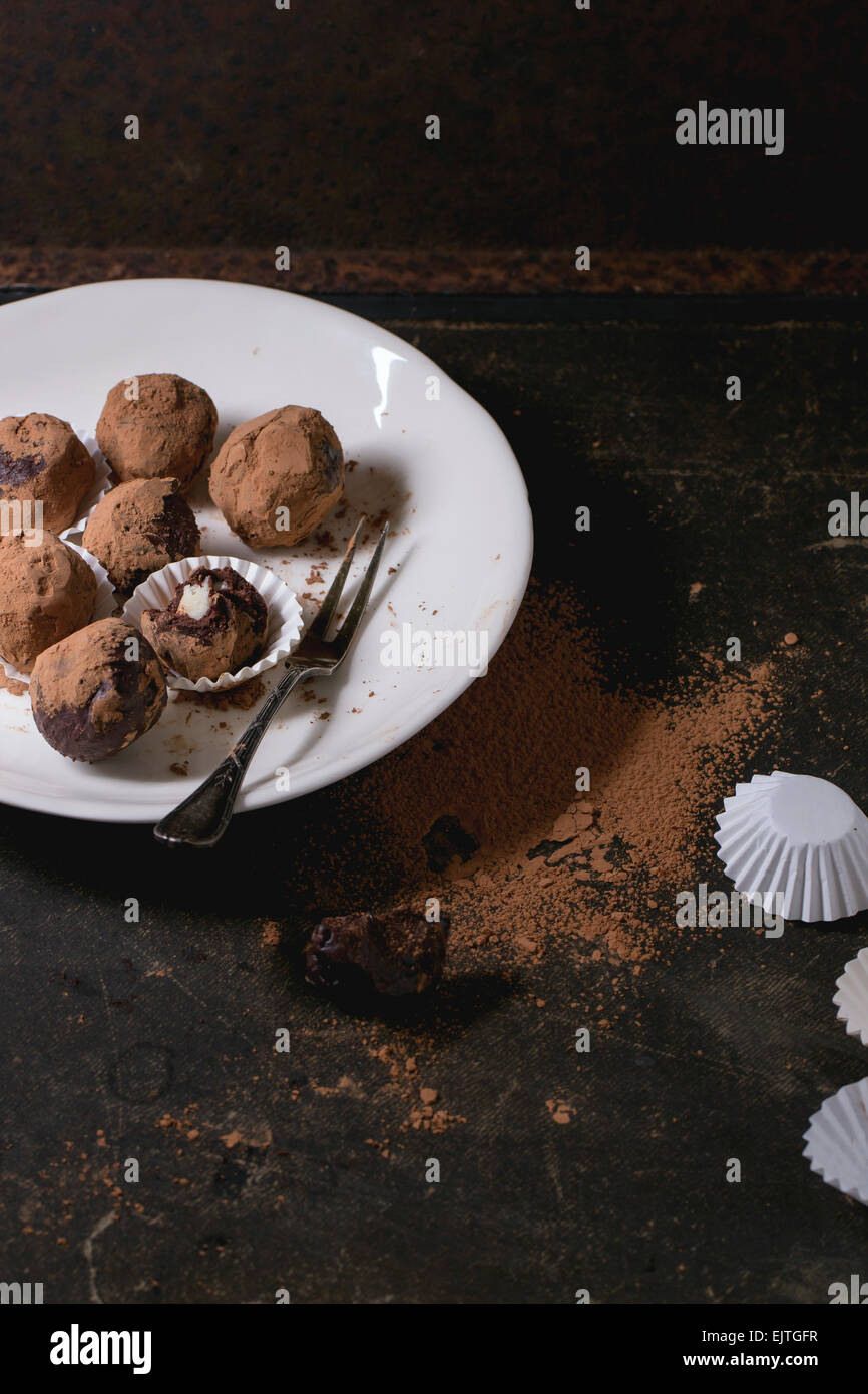 White plate with homemade chocolate truffles with marzipan and cocoa powder over dark table. Stock Photo
